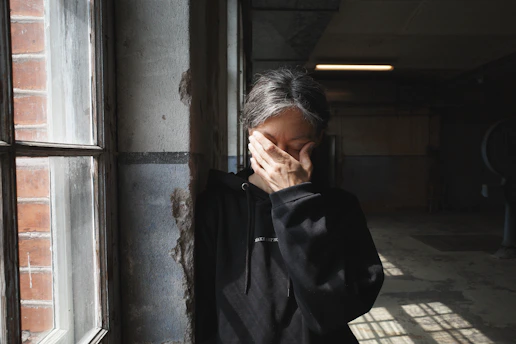 Person covers face with hand near window