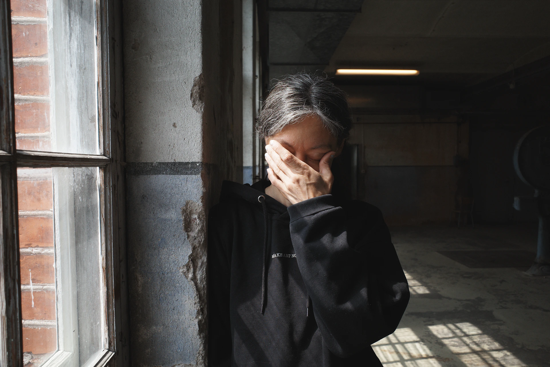 Person covers face with hand near window.