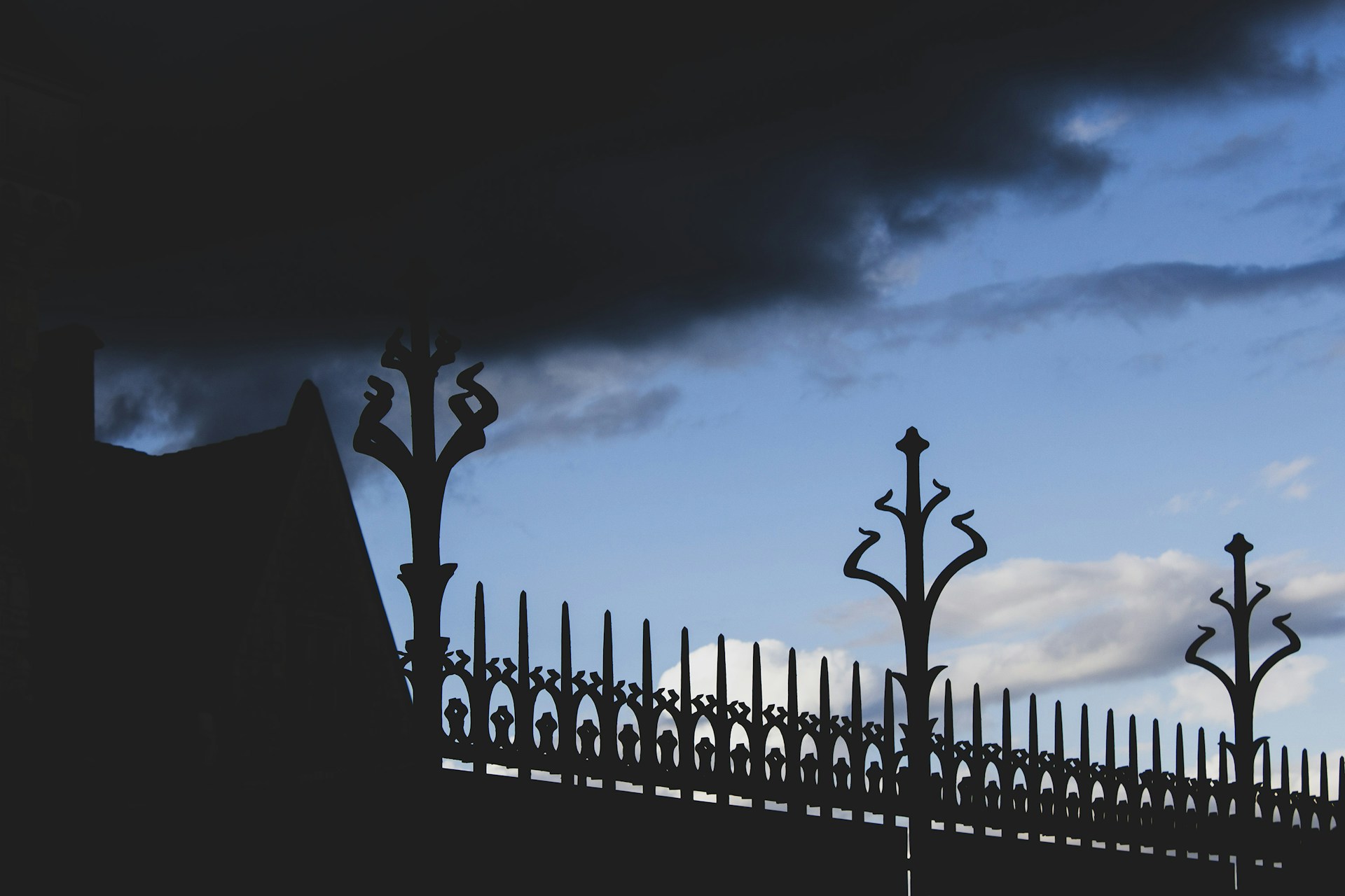 Silhouette of ornate fence against cloudy sky