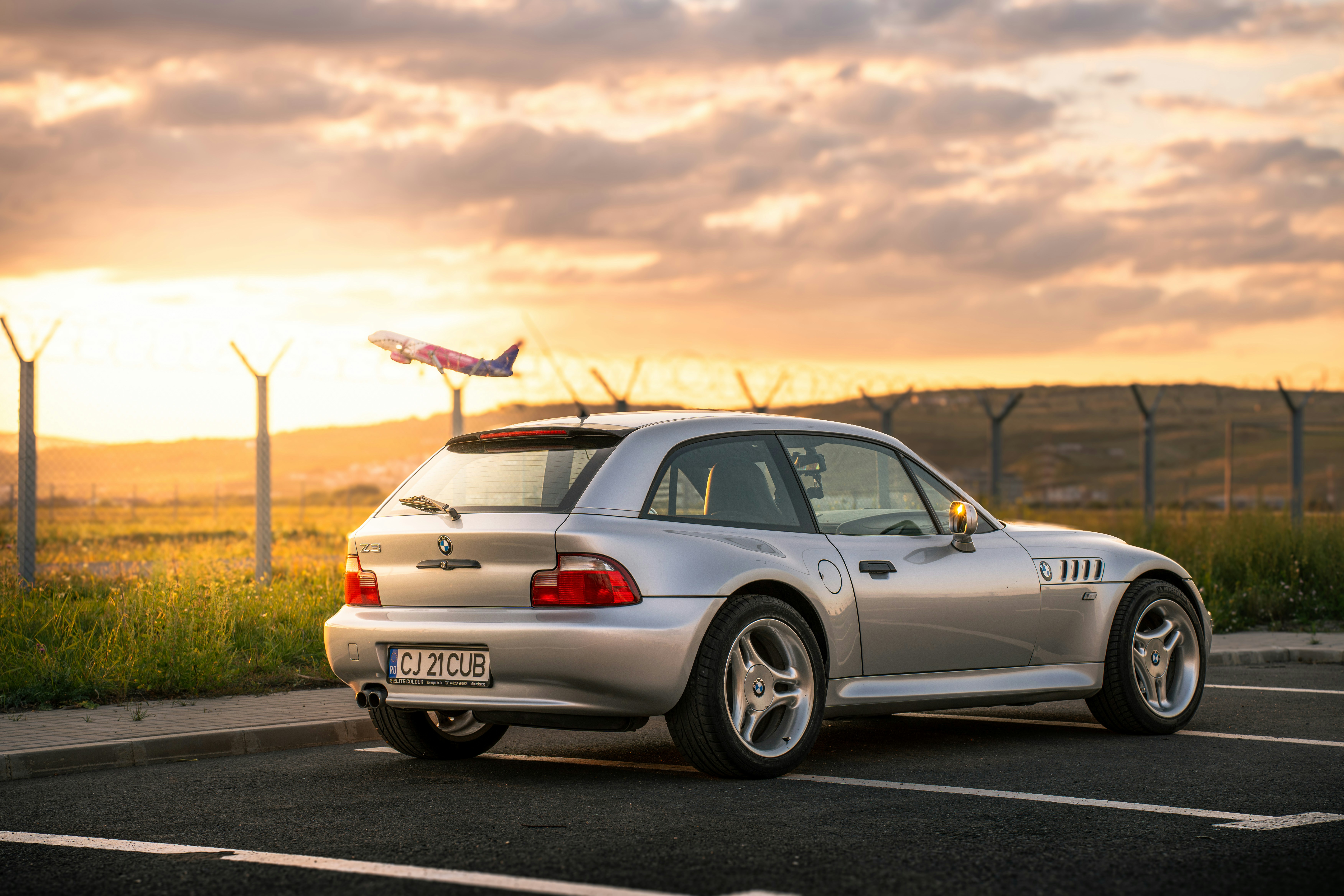 Silver coupe car parked near airport runway at sunset