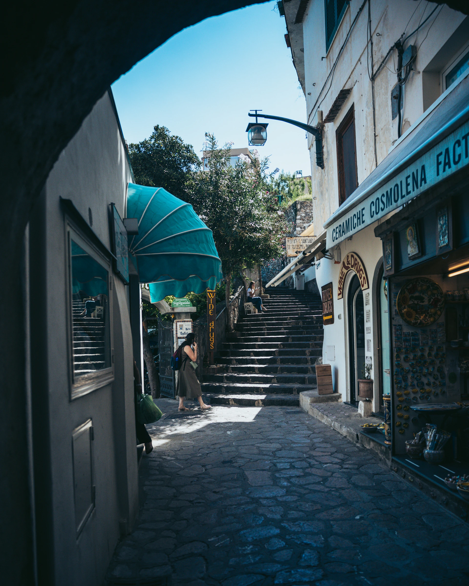Woman walking up sunlit stone steps in narrow alley.