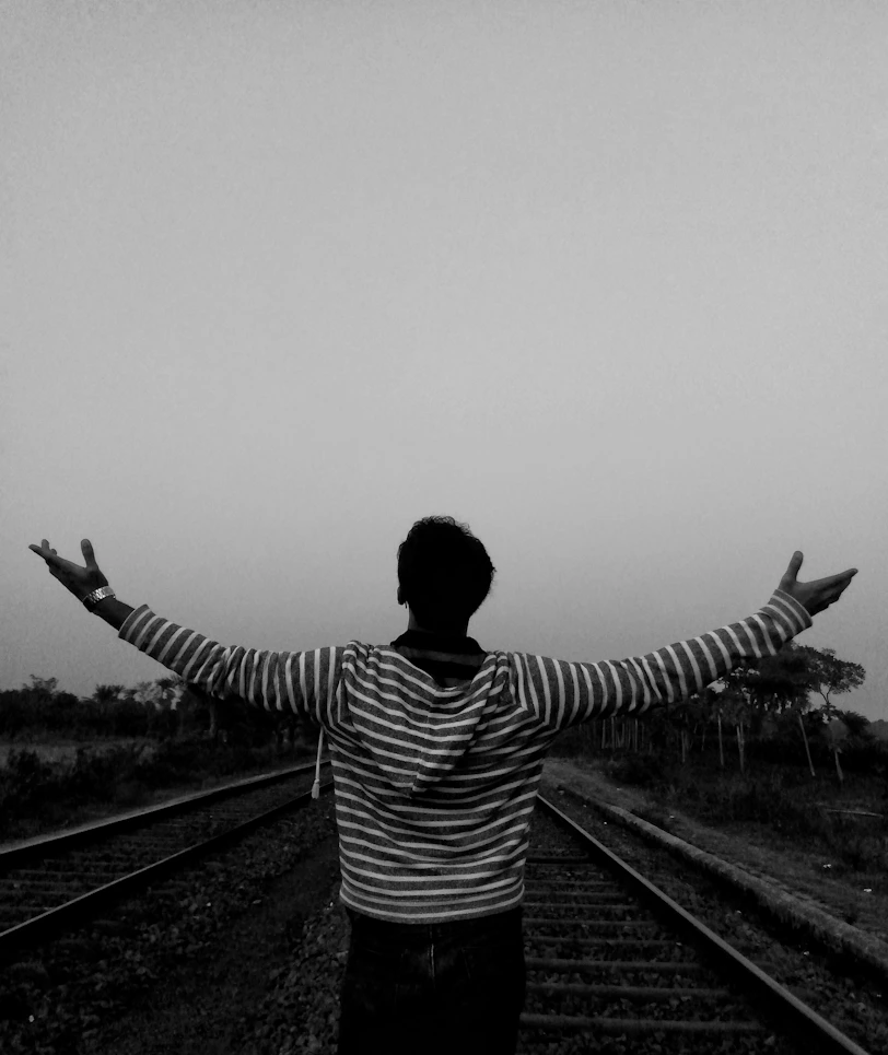 Man with arms outstretched on railroad tracks