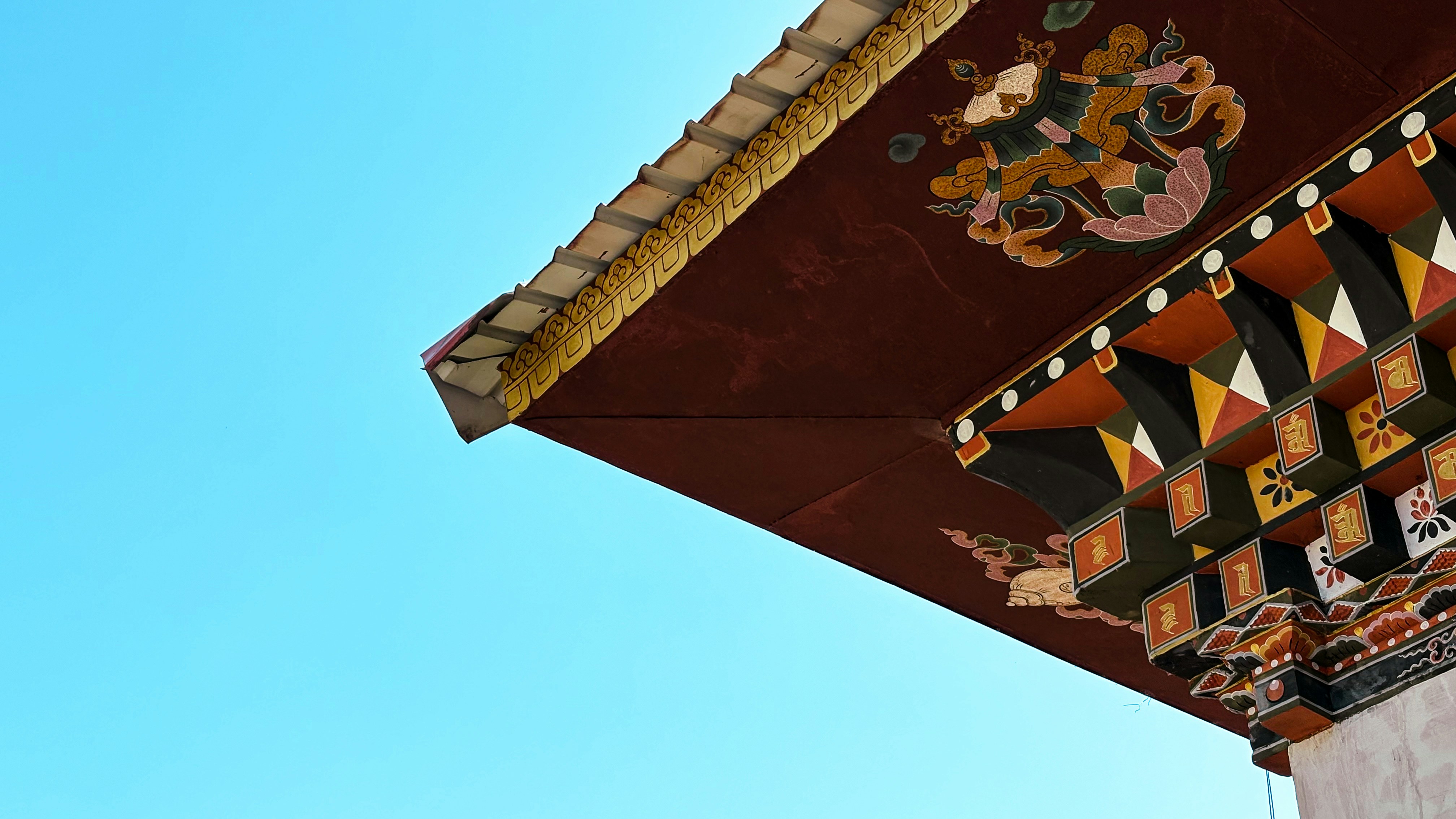 A close-up of an intricately painted Bhutanese roof in Thimphu contrasts vividly against a clear blue sky, highlighting the precision and artistry of traditional craftsmanship.