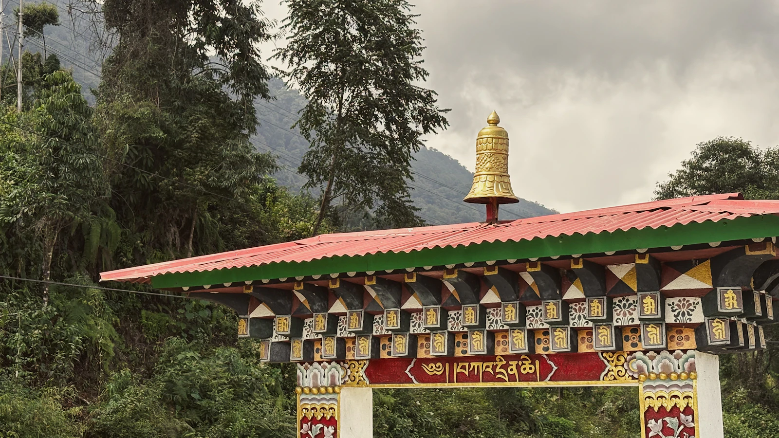 A painted Bhutanese archway crowned with a gilded bell at Phuentsholing, wooded hills rising behind