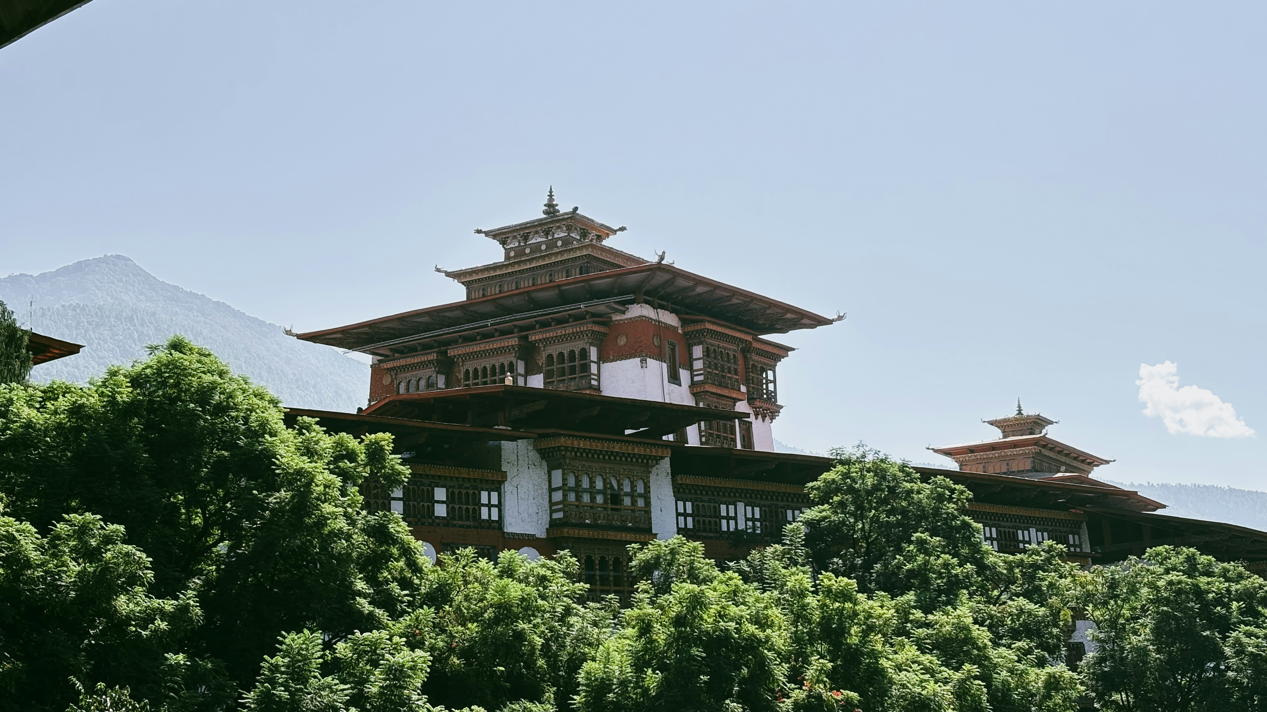 Traditional bhutanese architecture with ornate rooftops and trees.