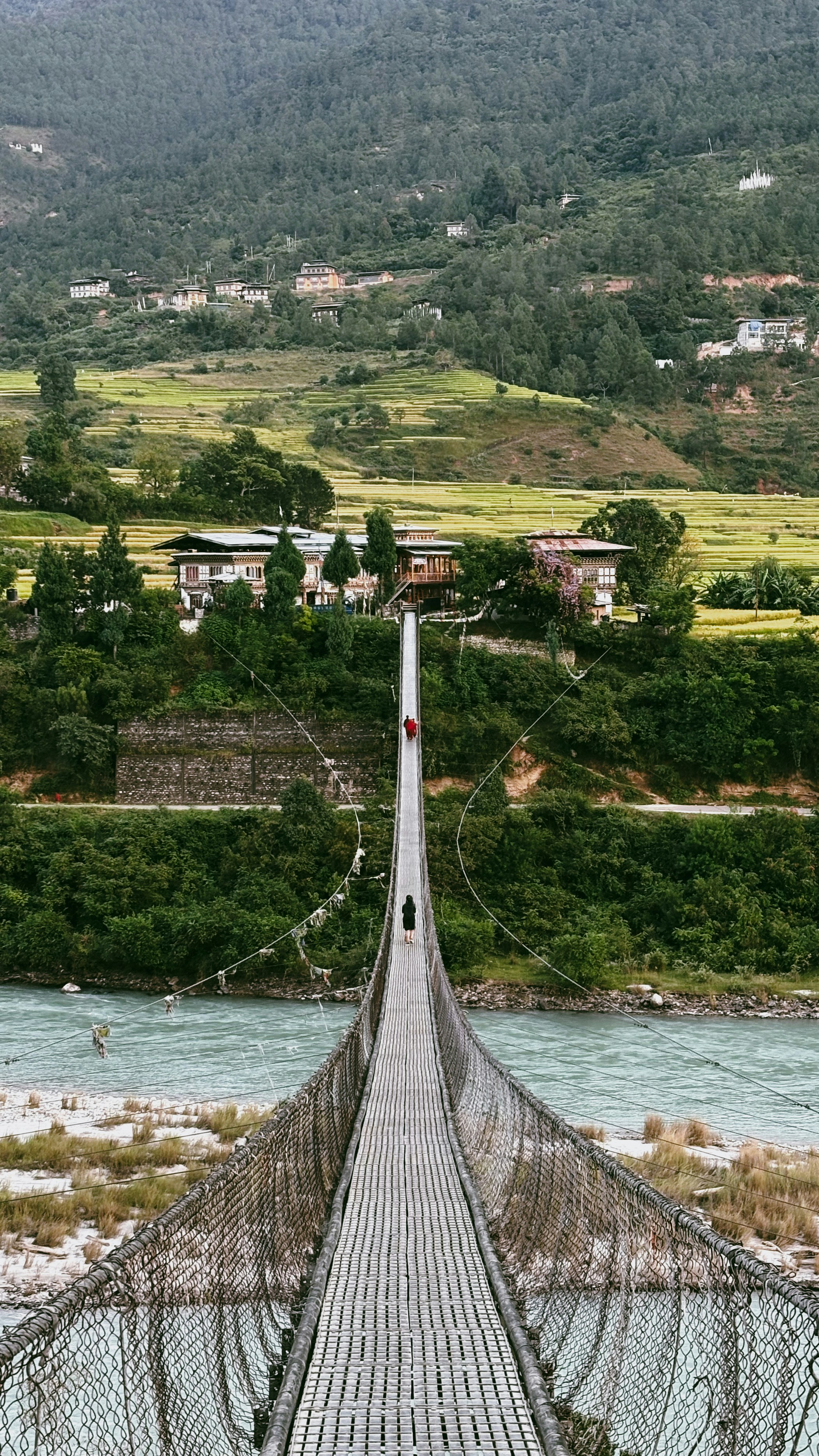 Suspension bridge over a river with lush green hills.