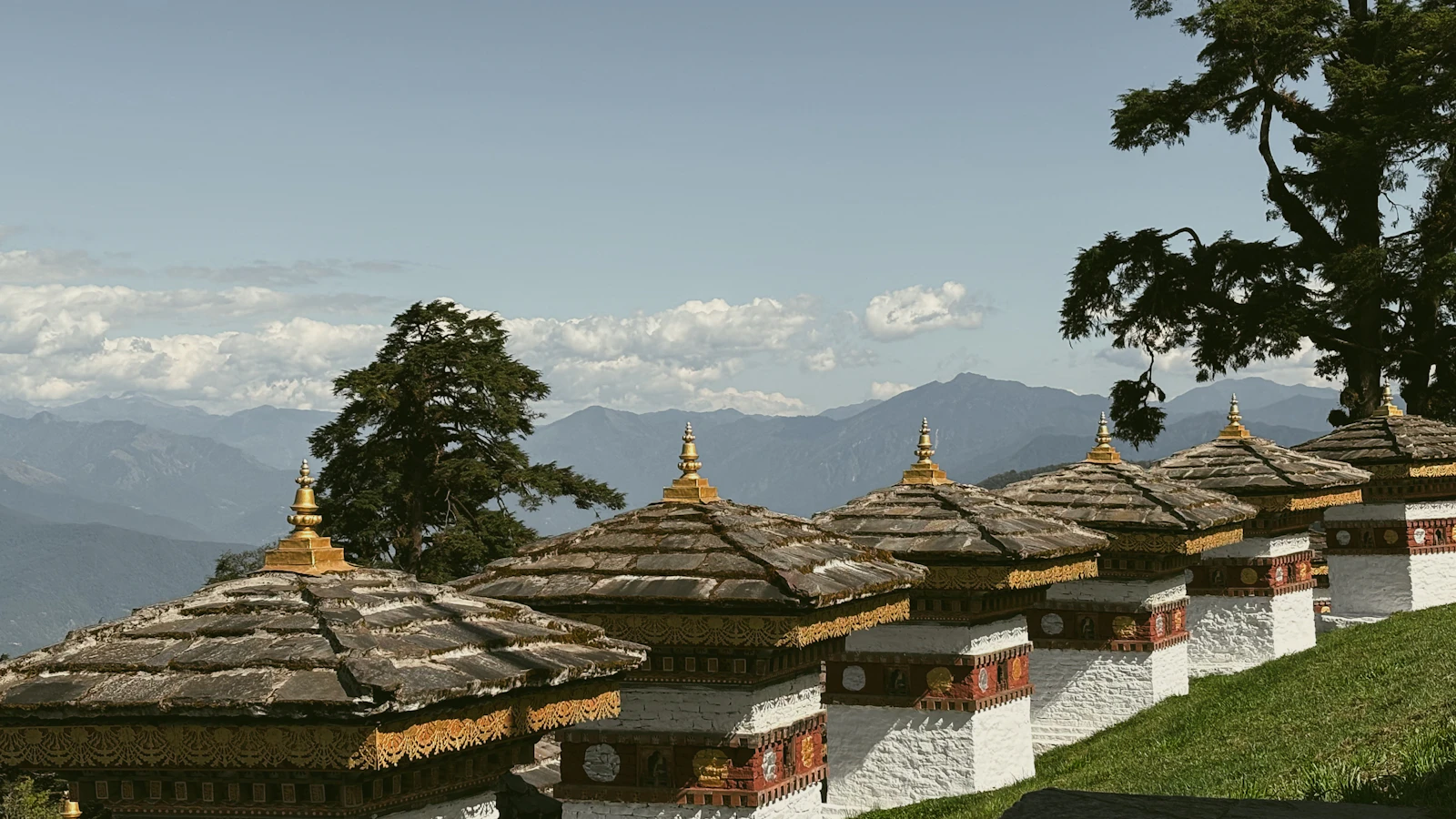 A row of the Druk Wangyal chortens at Dochu La on a grassy rise, with blue mountain ridges beyond