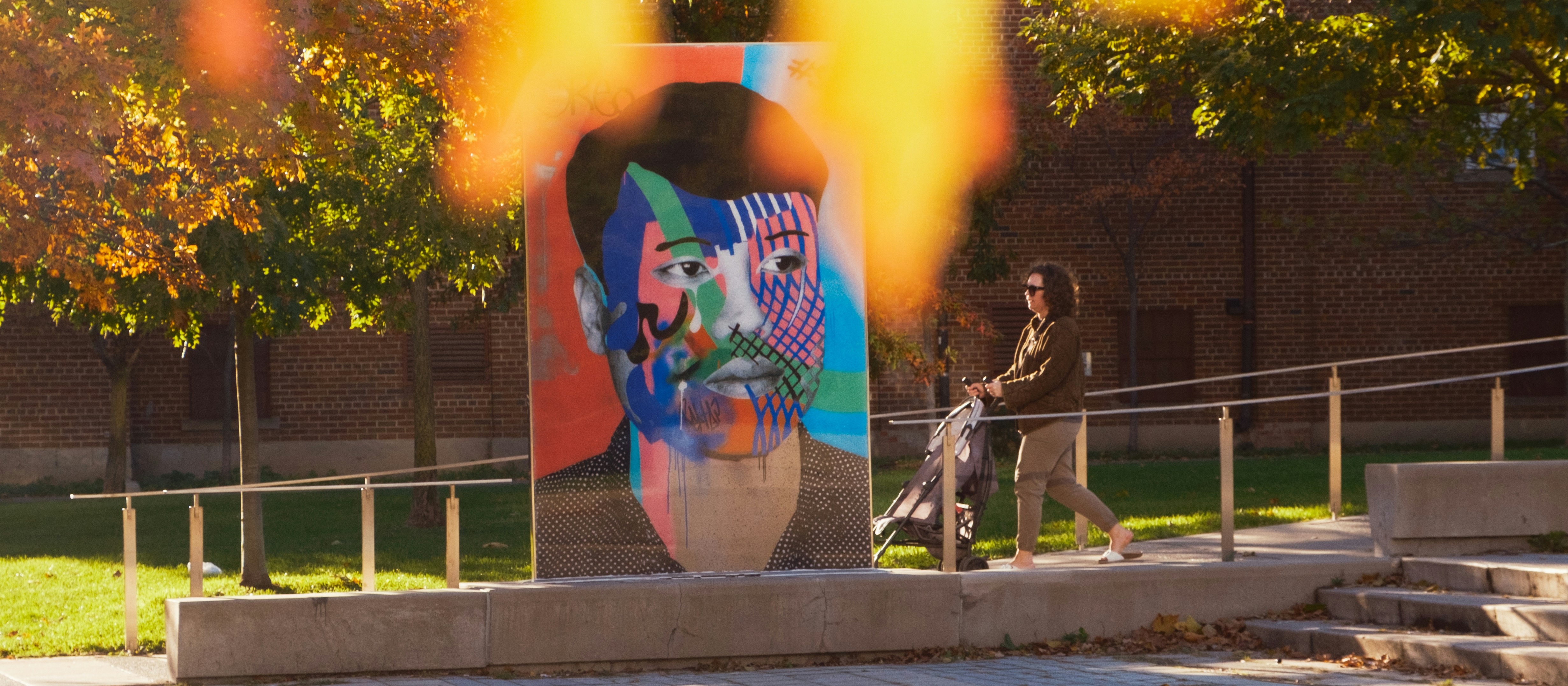 La femme pousse la poussette devant la fresque colorée d’un visage.