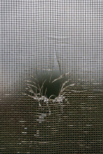 A torn window screen with a hole in it