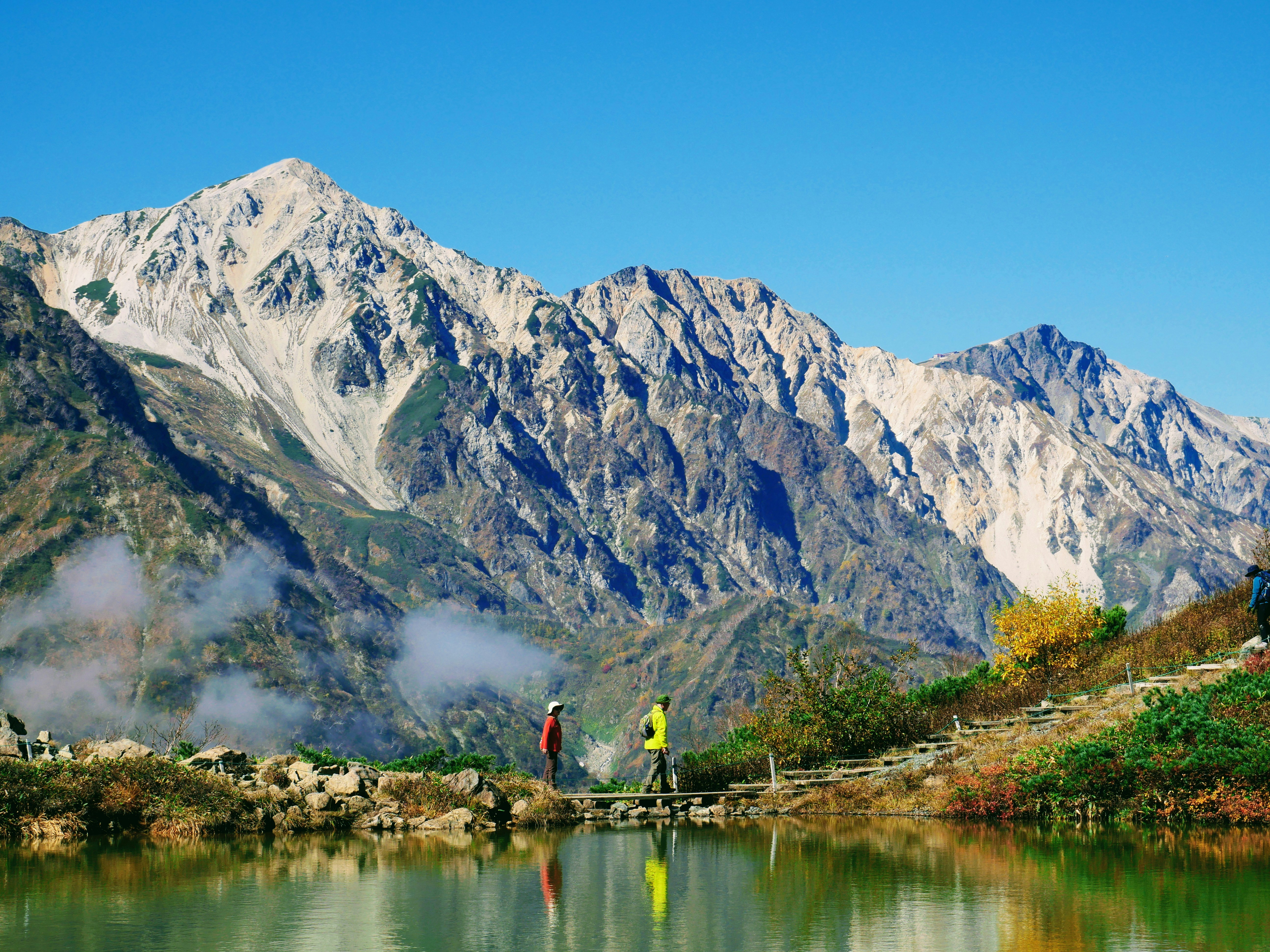 Two hikers by a lake with majestic mountains behind.