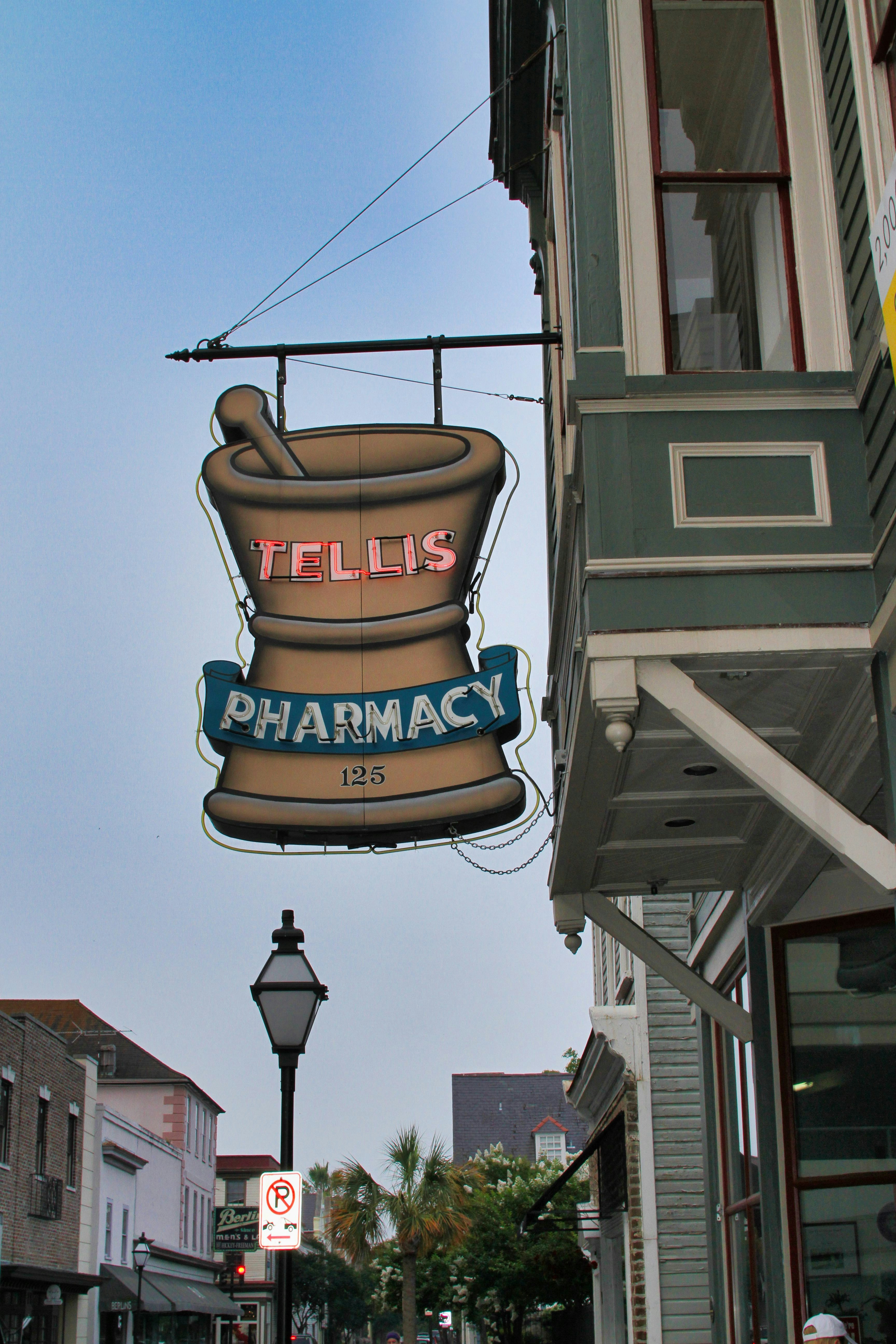 A vintage pharmacy sign hangs outside a building.