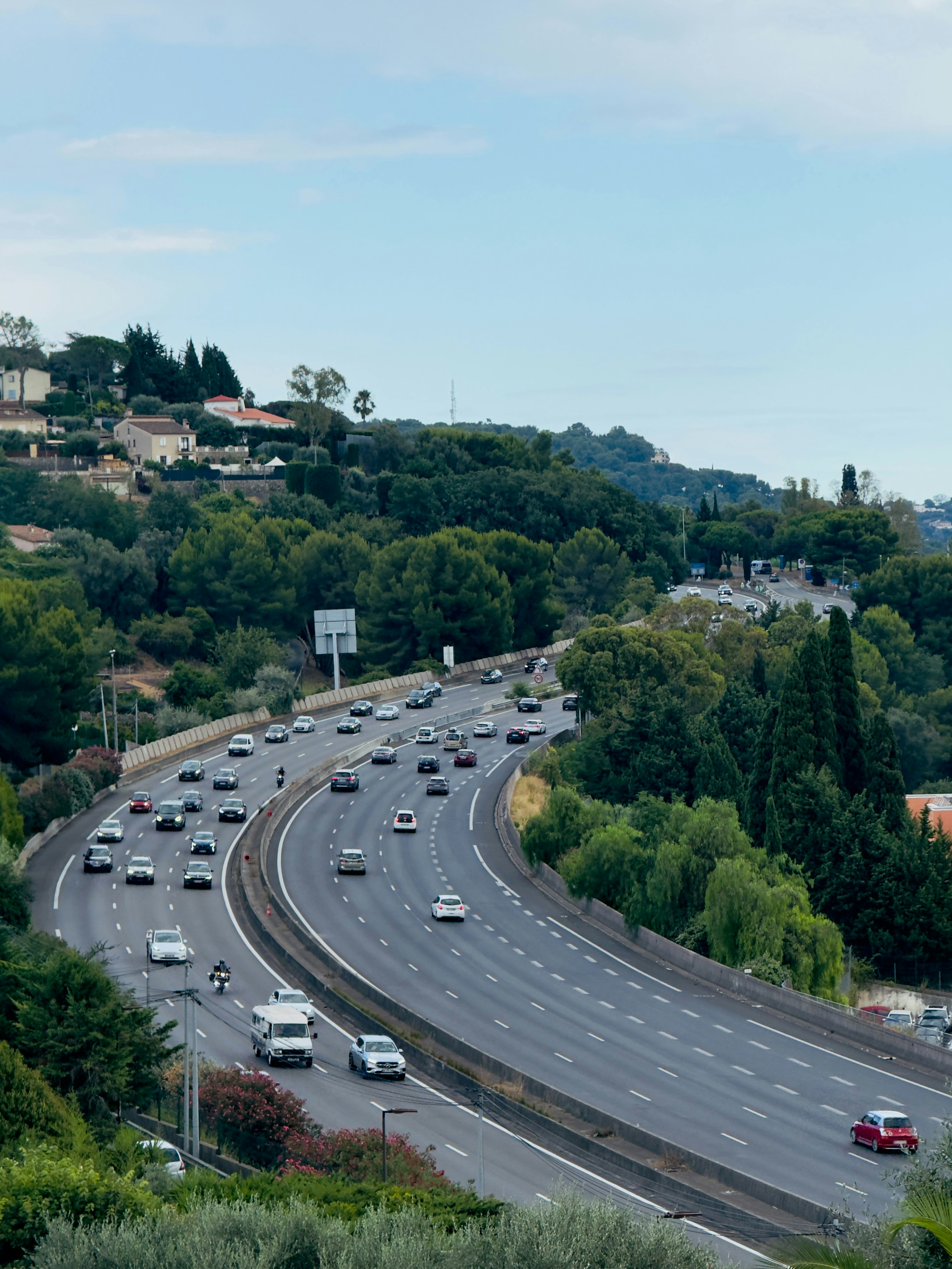 Cars driving on a curved highway through green hills.