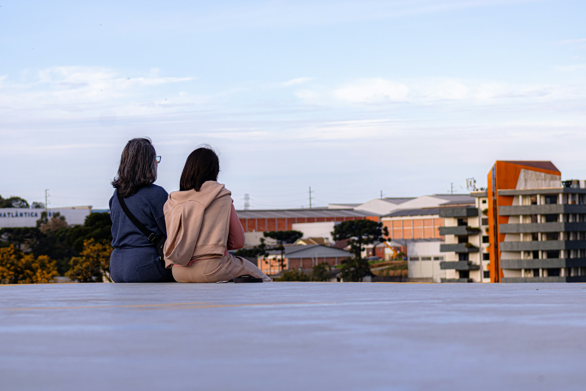 Two women sit on rooftop overlooking city buildings