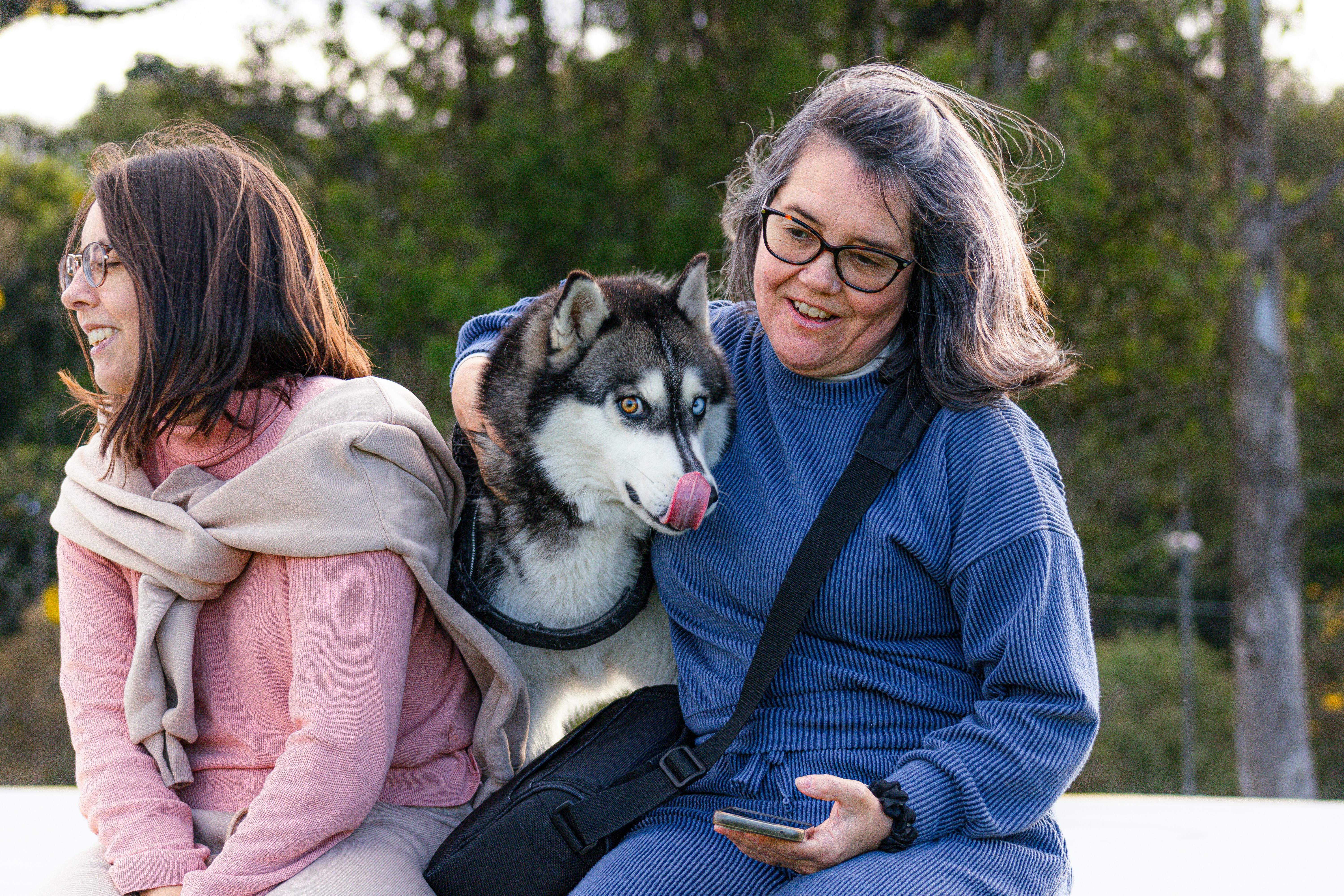 Two women and a husky dog sitting together outside.