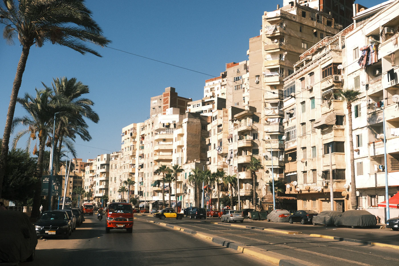 Apartment buildings lined along a street with palm trees between them