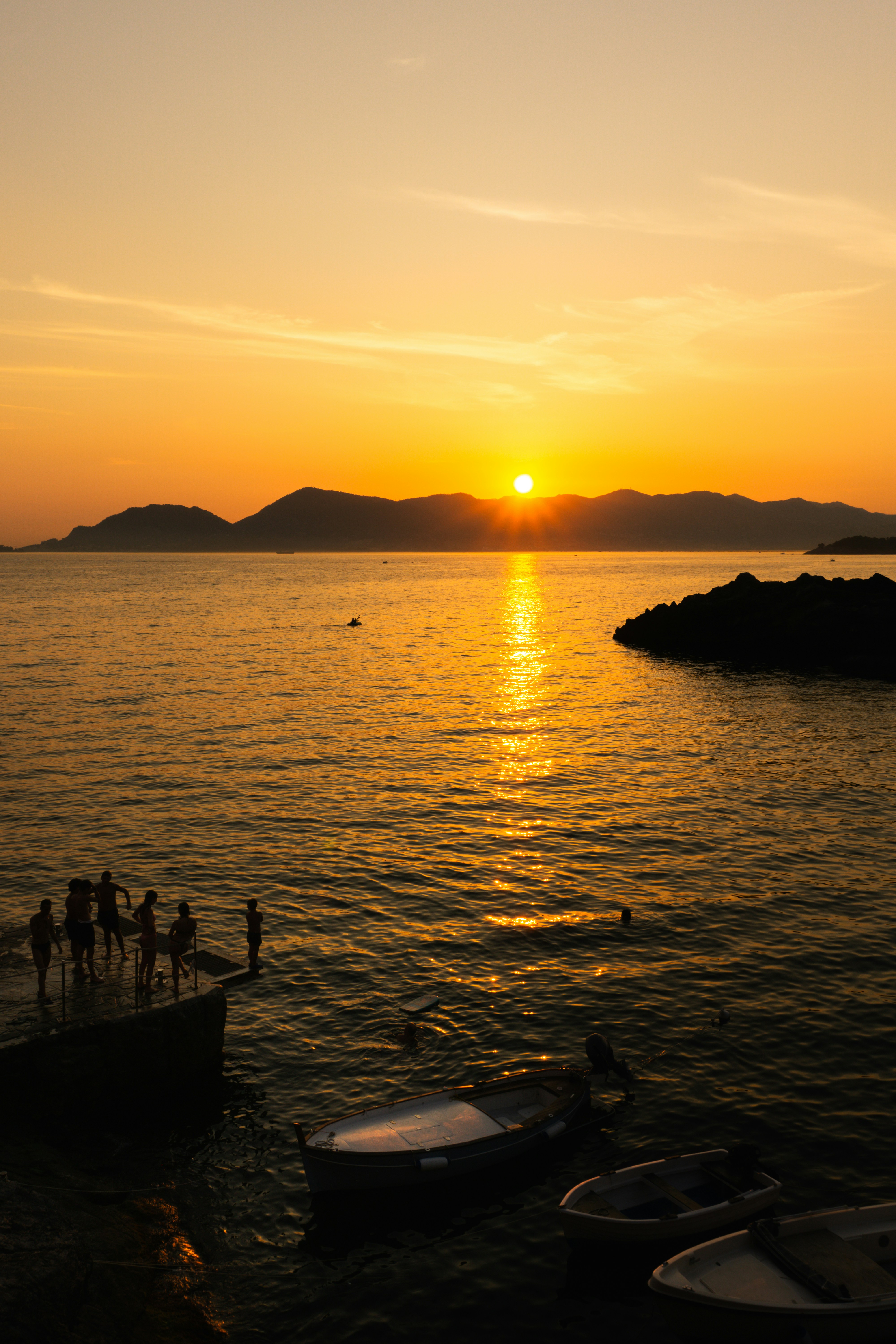 Sunset over the ocean with people on a dock.