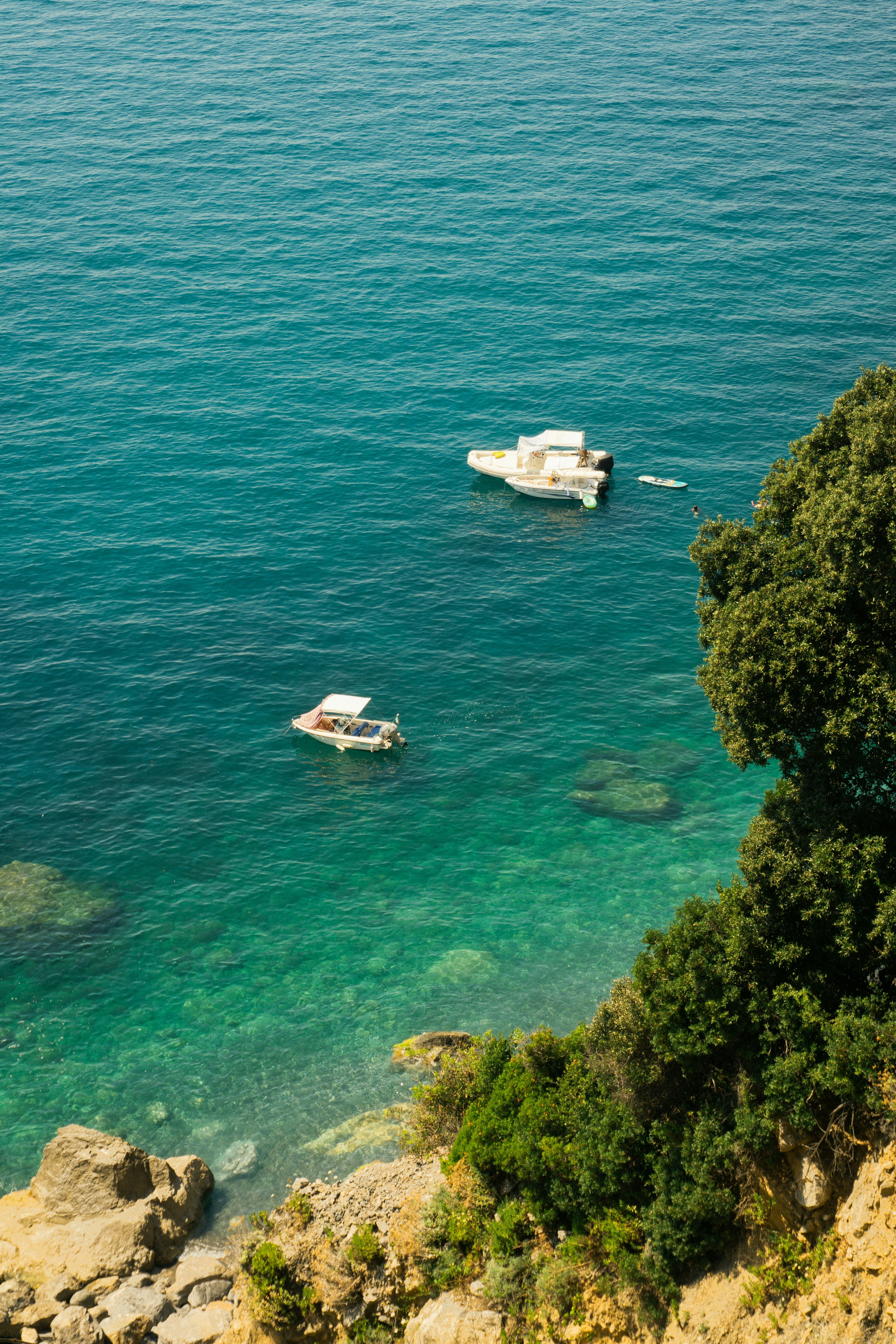 Two boats float on clear turquoise water near rocky shore.