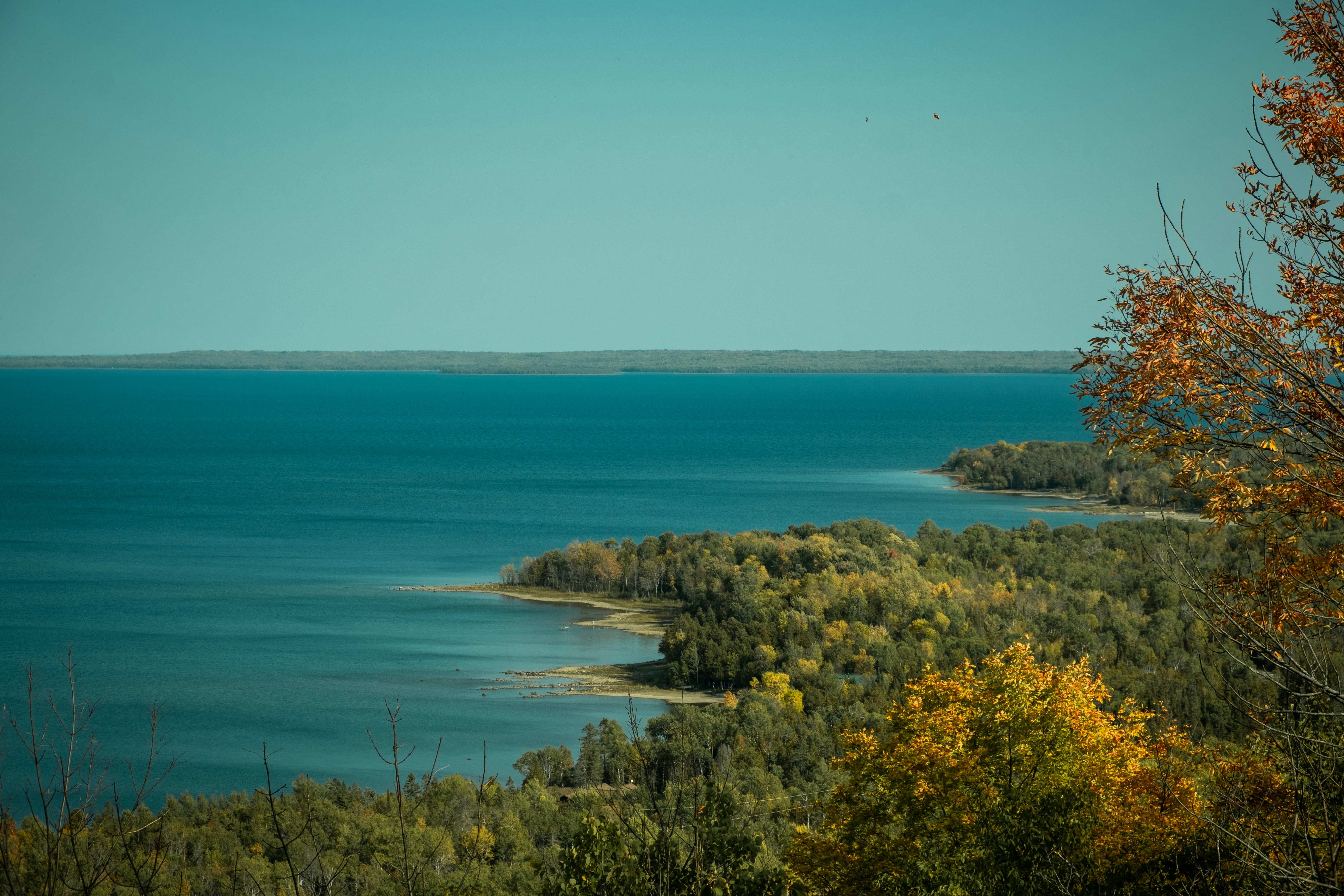 Vast blue lake bordered by lush green and yellow trees.