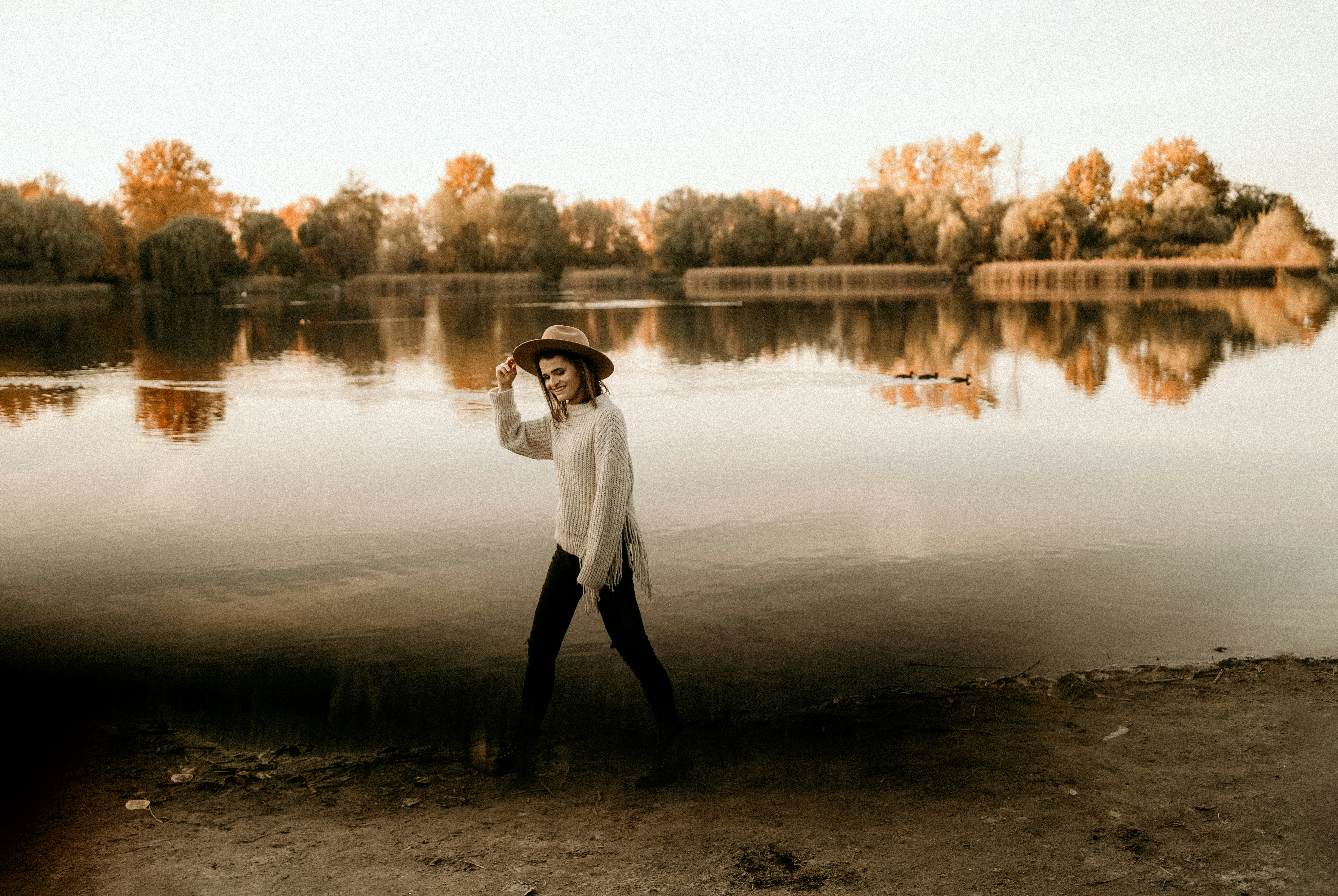 Woman in hat walks by a lake at sunset