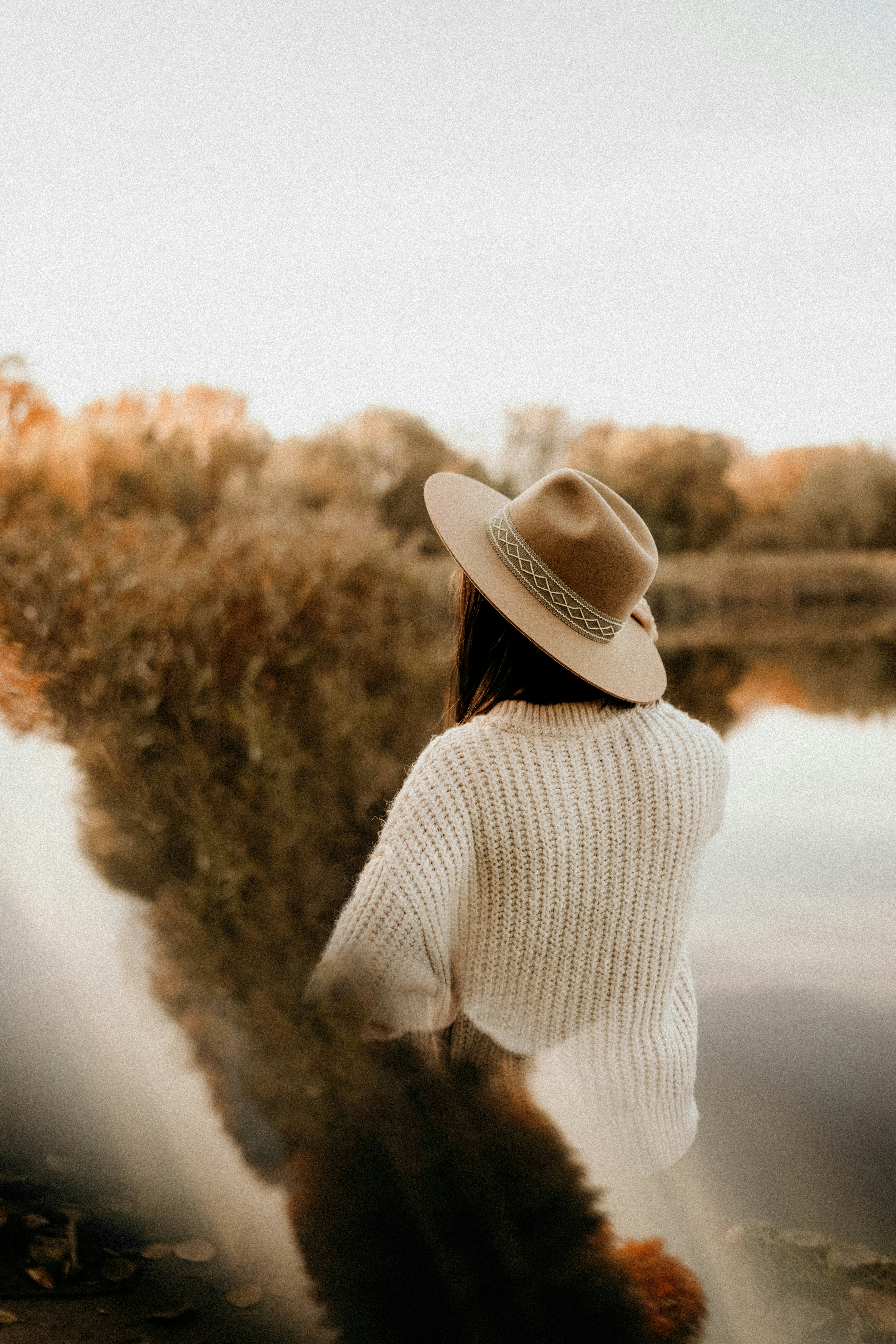 Woman in hat and sweater by a calm lake