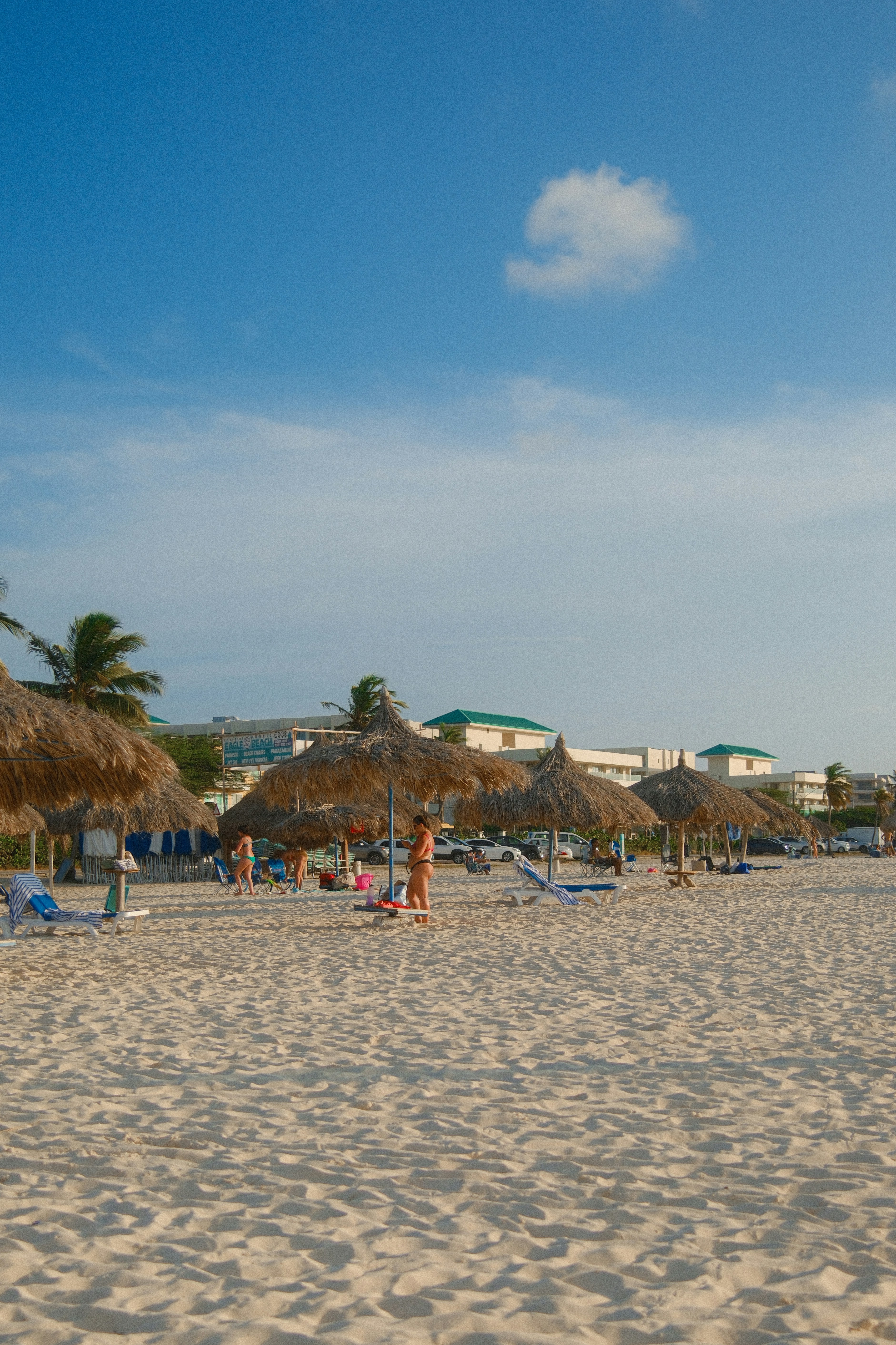Plage tropicale avec parasols et bâtiments au toit de chaume.