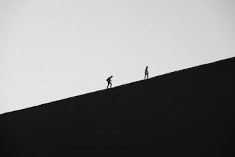 Two hikers ascend a dark, barren dune.