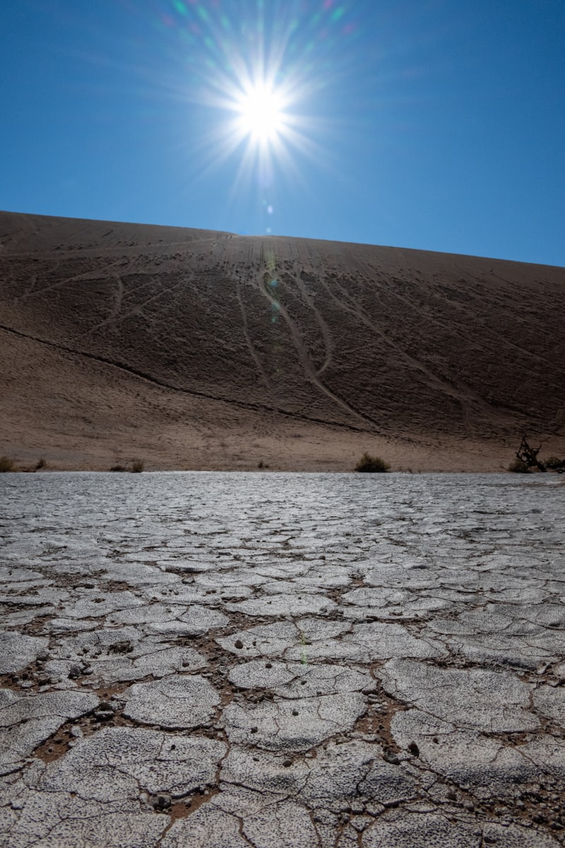 Bright sun shines over cracked earth and barren hill