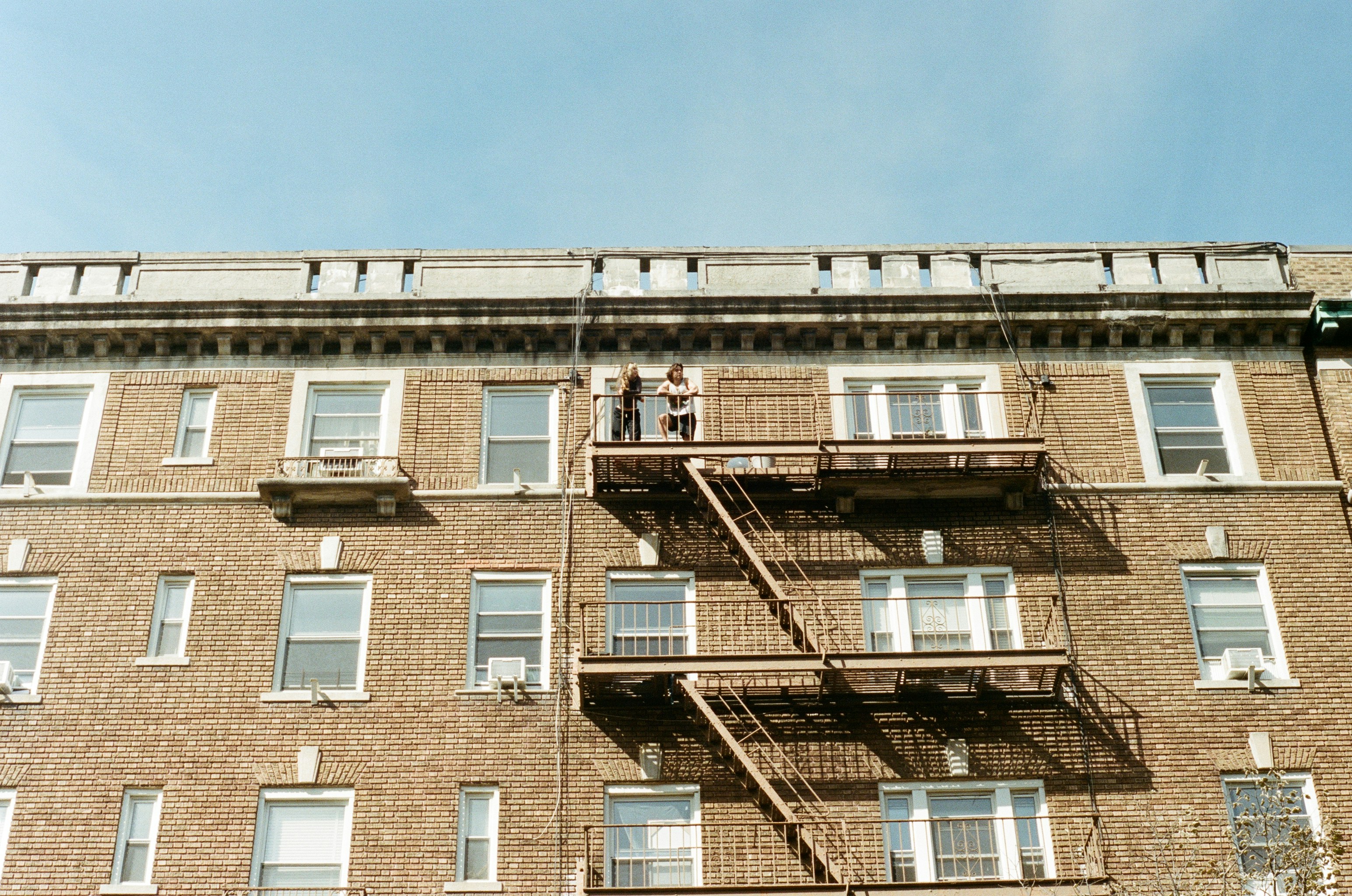 Two people on a fire escape of a brick building.
