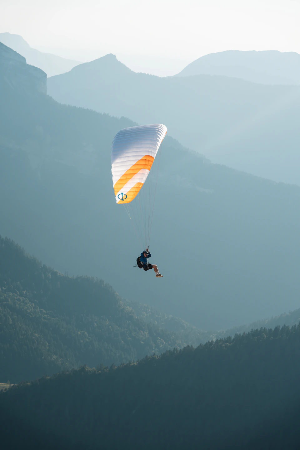Person paragliding over mountain range with orange and white parachute in mid-air