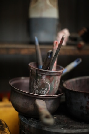 Paintbrushes in a metal pot with other supplies