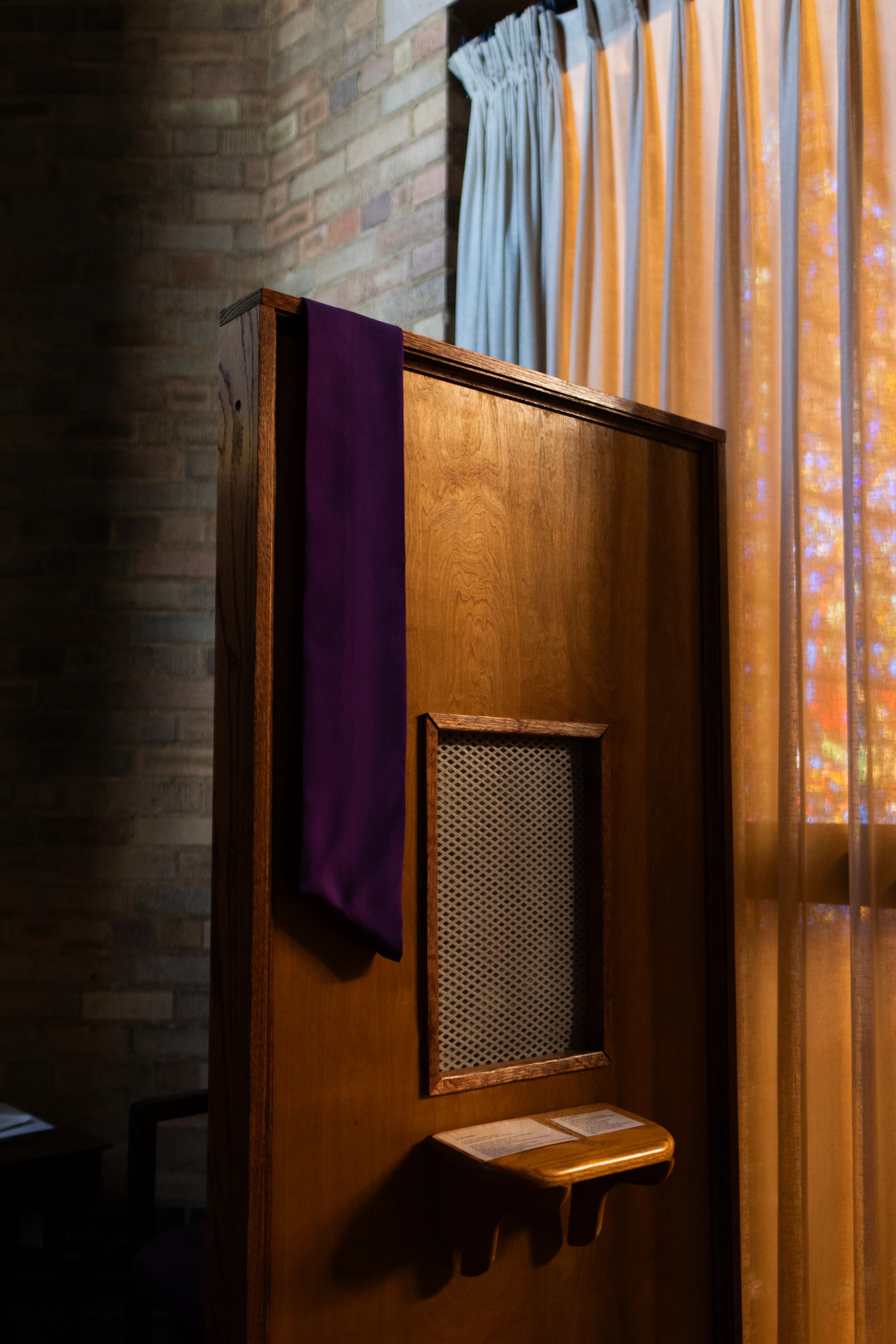Wooden confessional booth with purple stole and window.