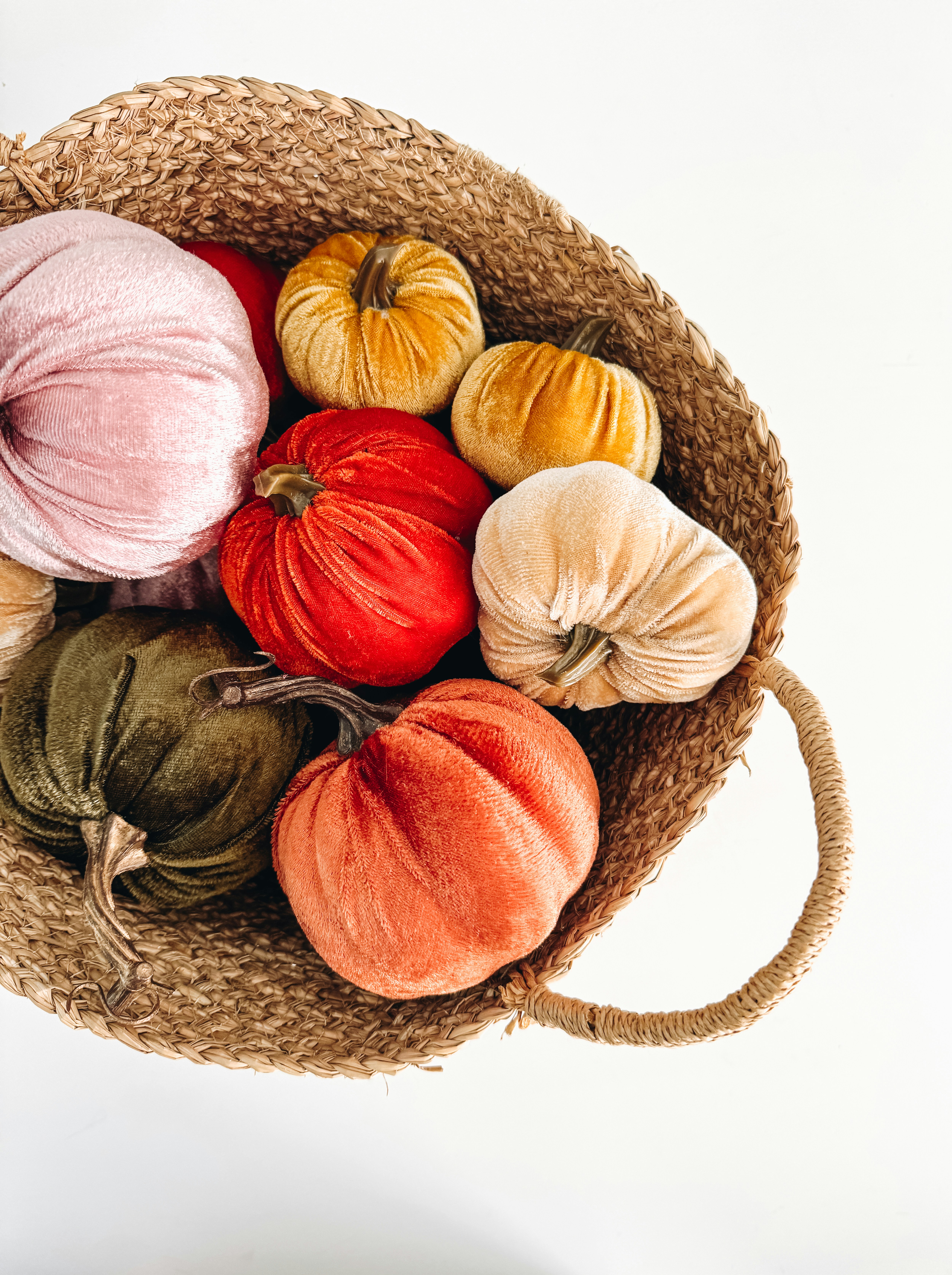 A woven basket filled with velvet pumpkins of various colors.