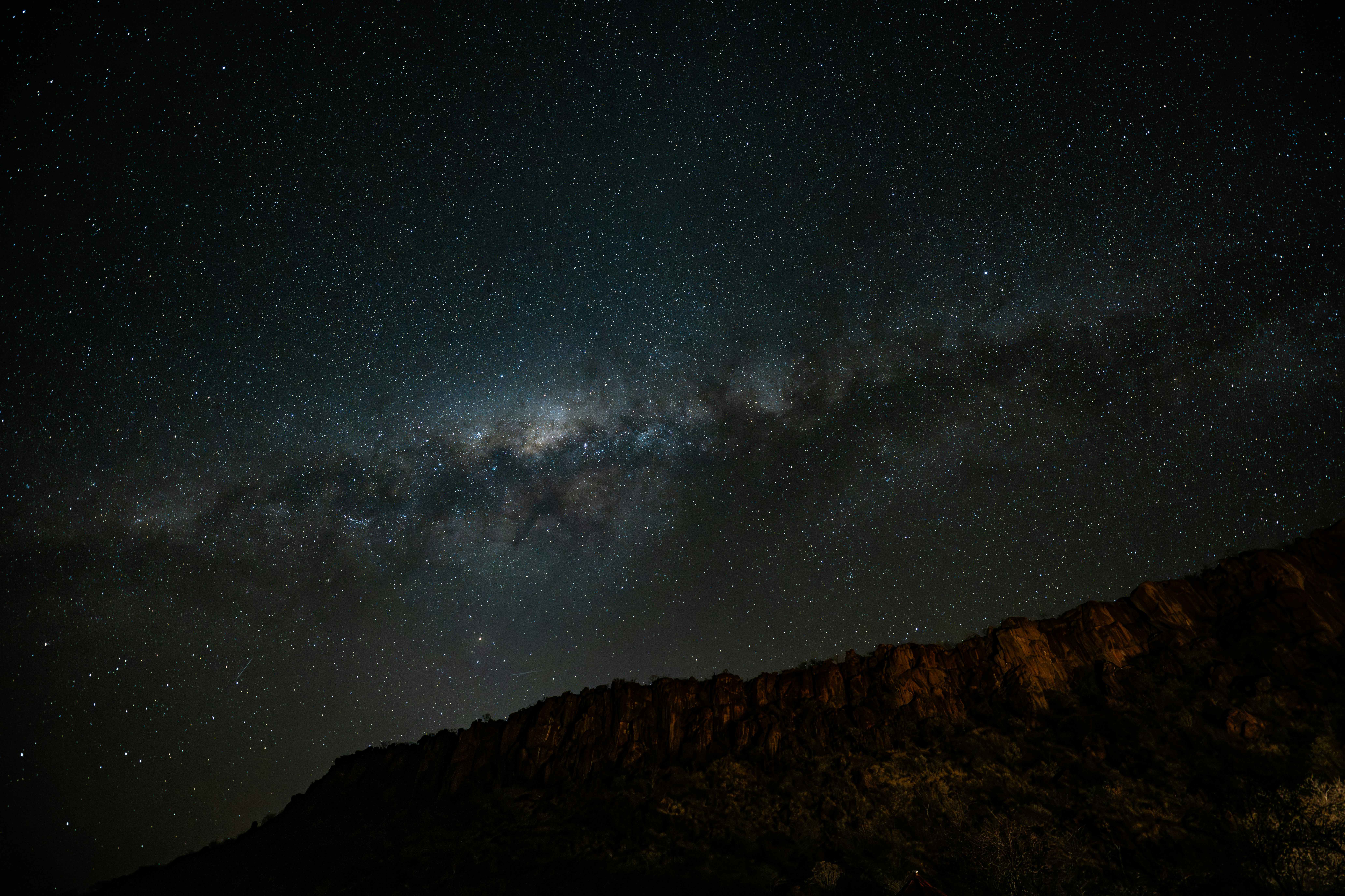 The milky way galaxy arches over a dark mountain range.