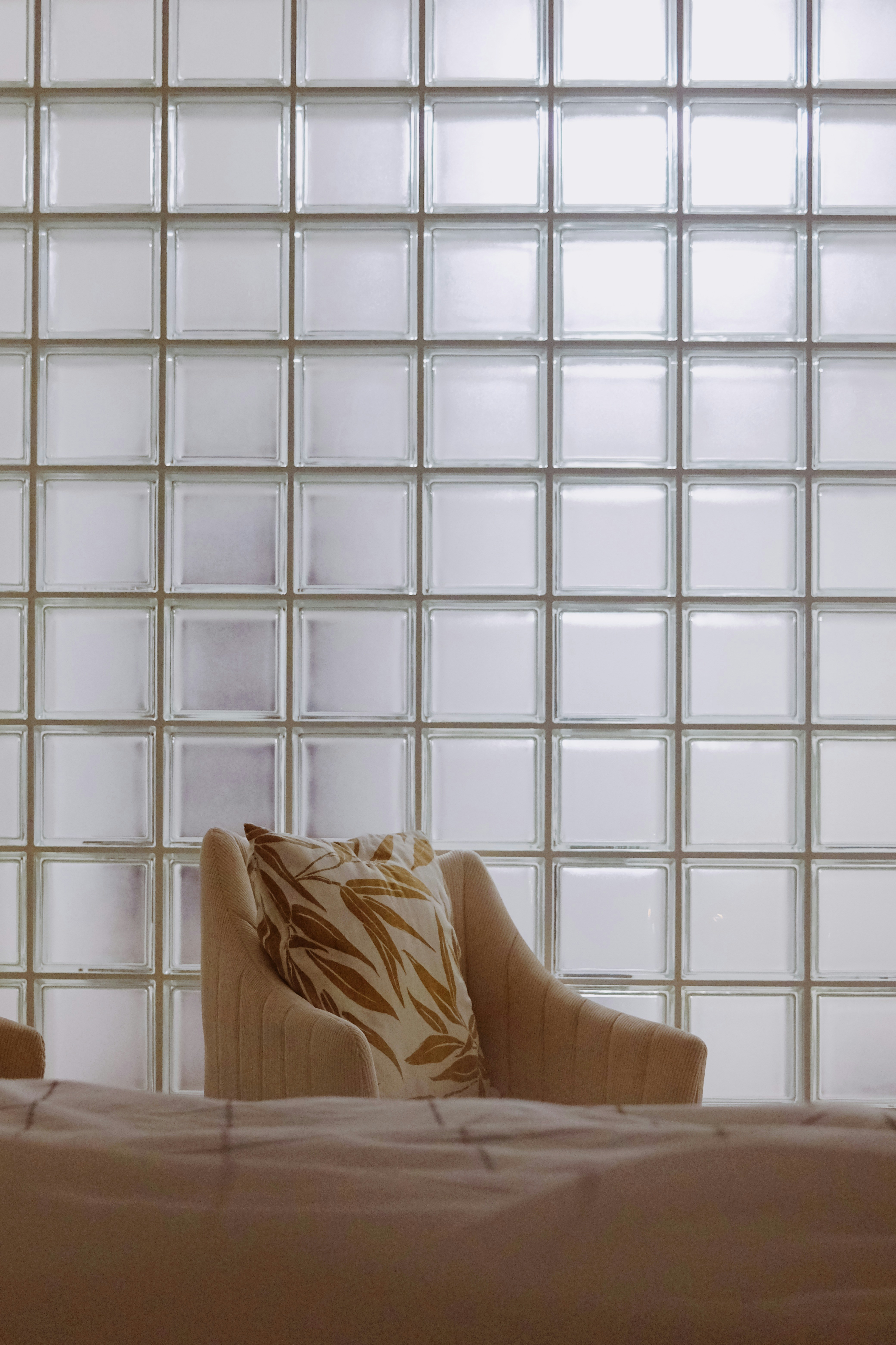 Armchair with patterned pillow against glass block wall