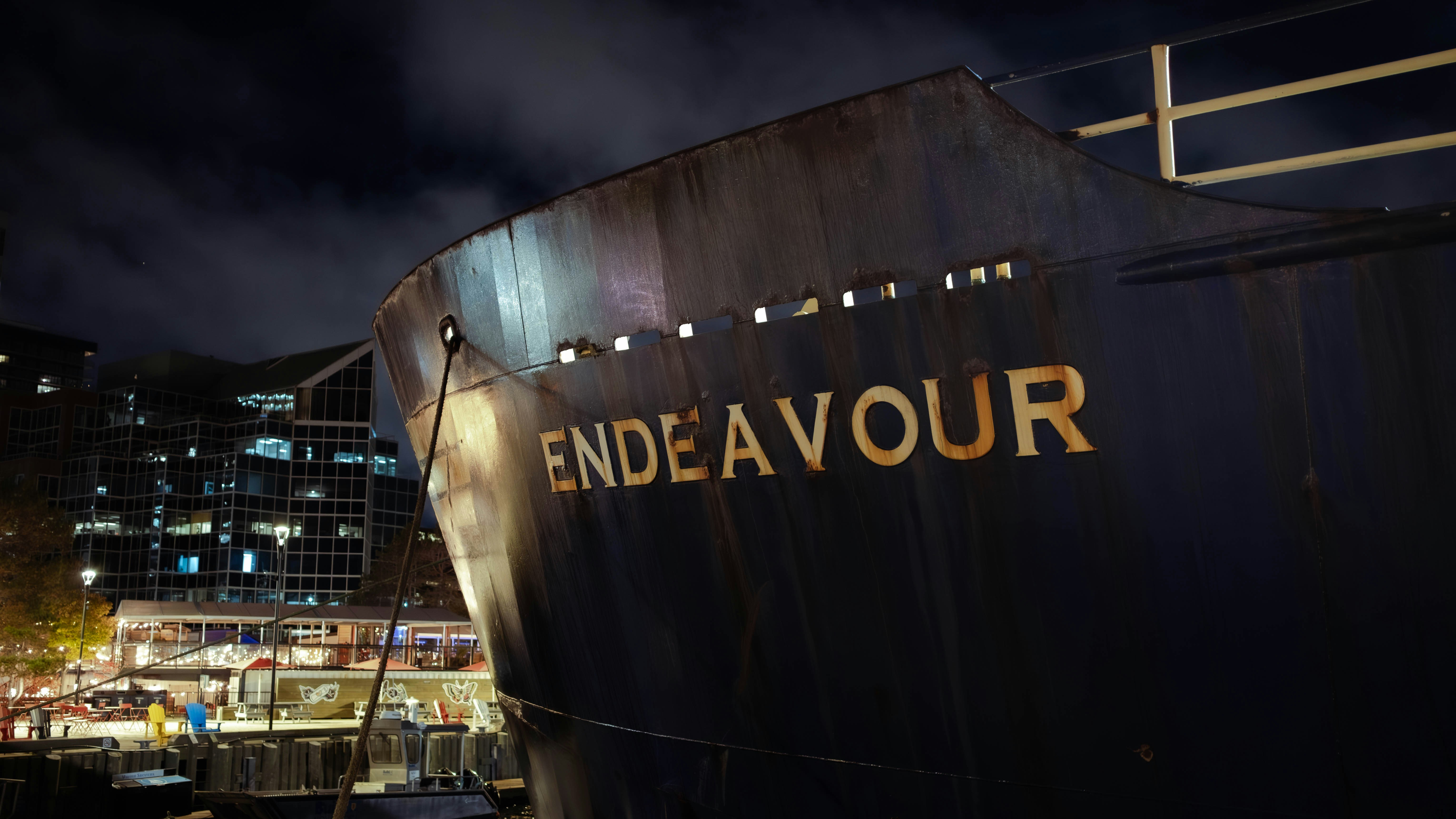 Ship named endeavour docked at night in a city.