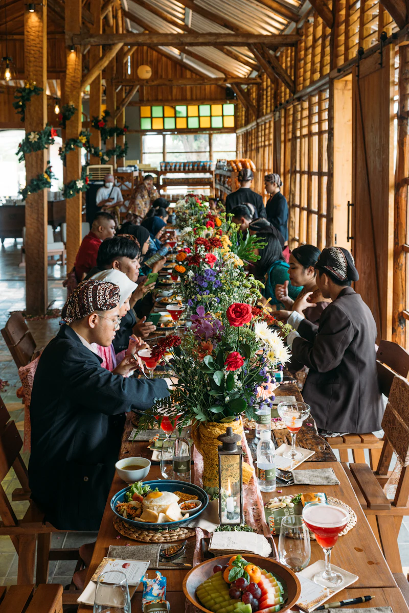 People sitting along a long shared table with flowers and plates of food
