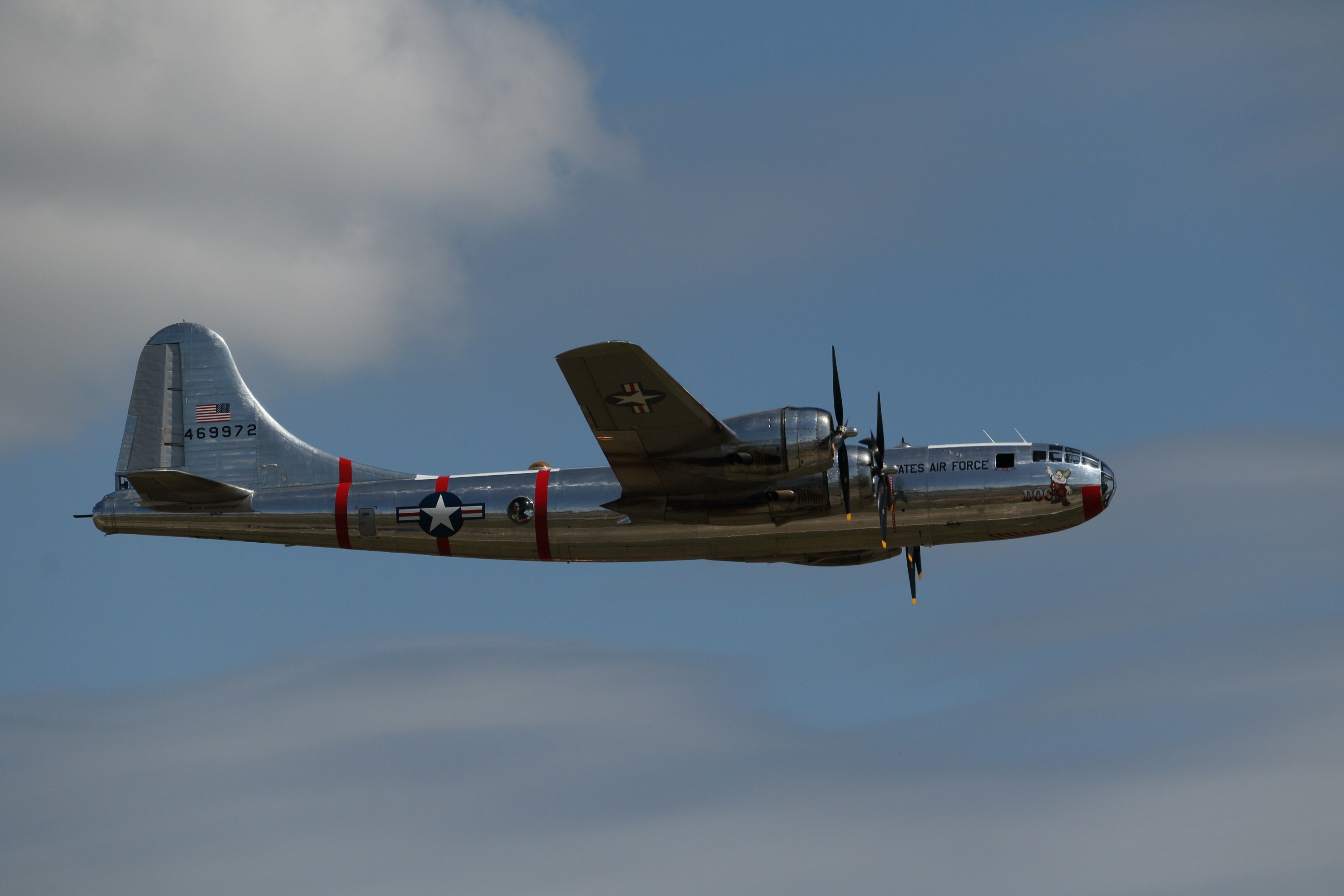 A vintage silver bomber airplane flying in the sky.