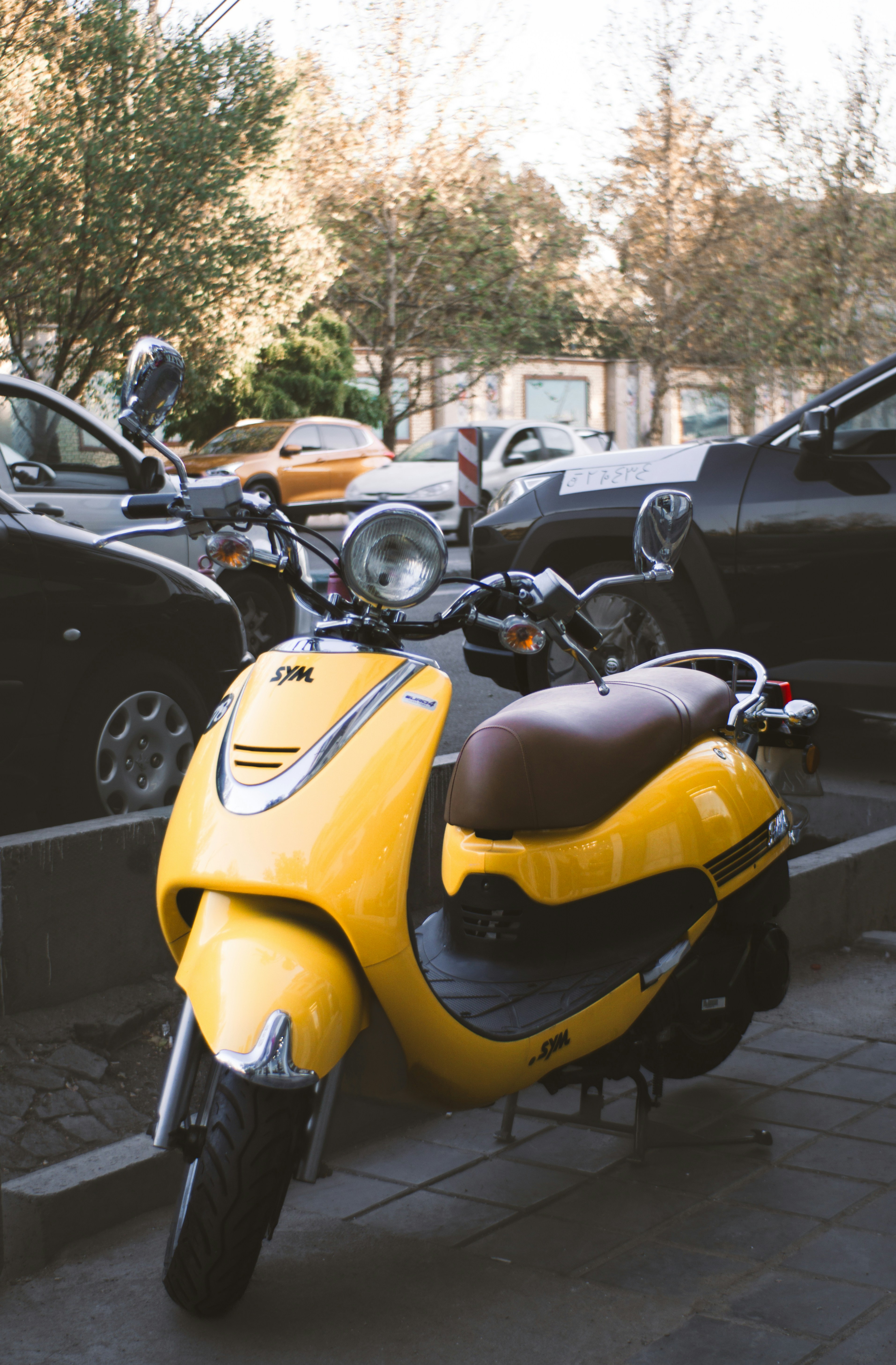 A bright yellow scooter parked on a city sidewalk.