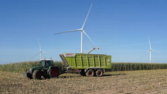 Tractor harvesting corn field with wind turbines