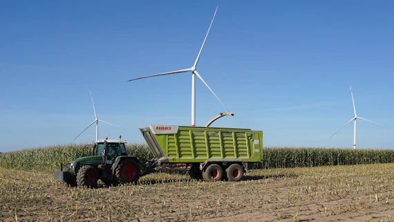 Tractor harvesting corn field with wind turbines