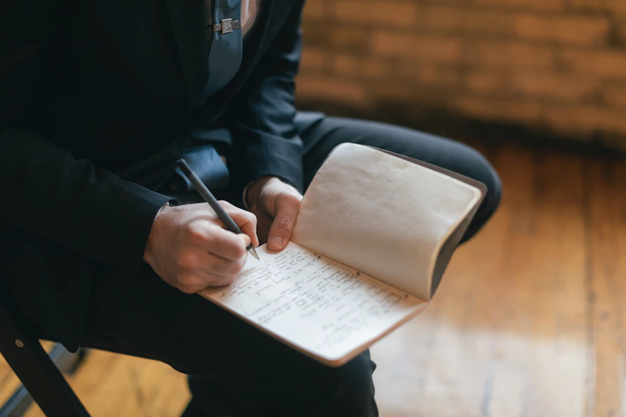An adult writes by hand in an open notebook while seated, working through thoughts on paper in soft warm light