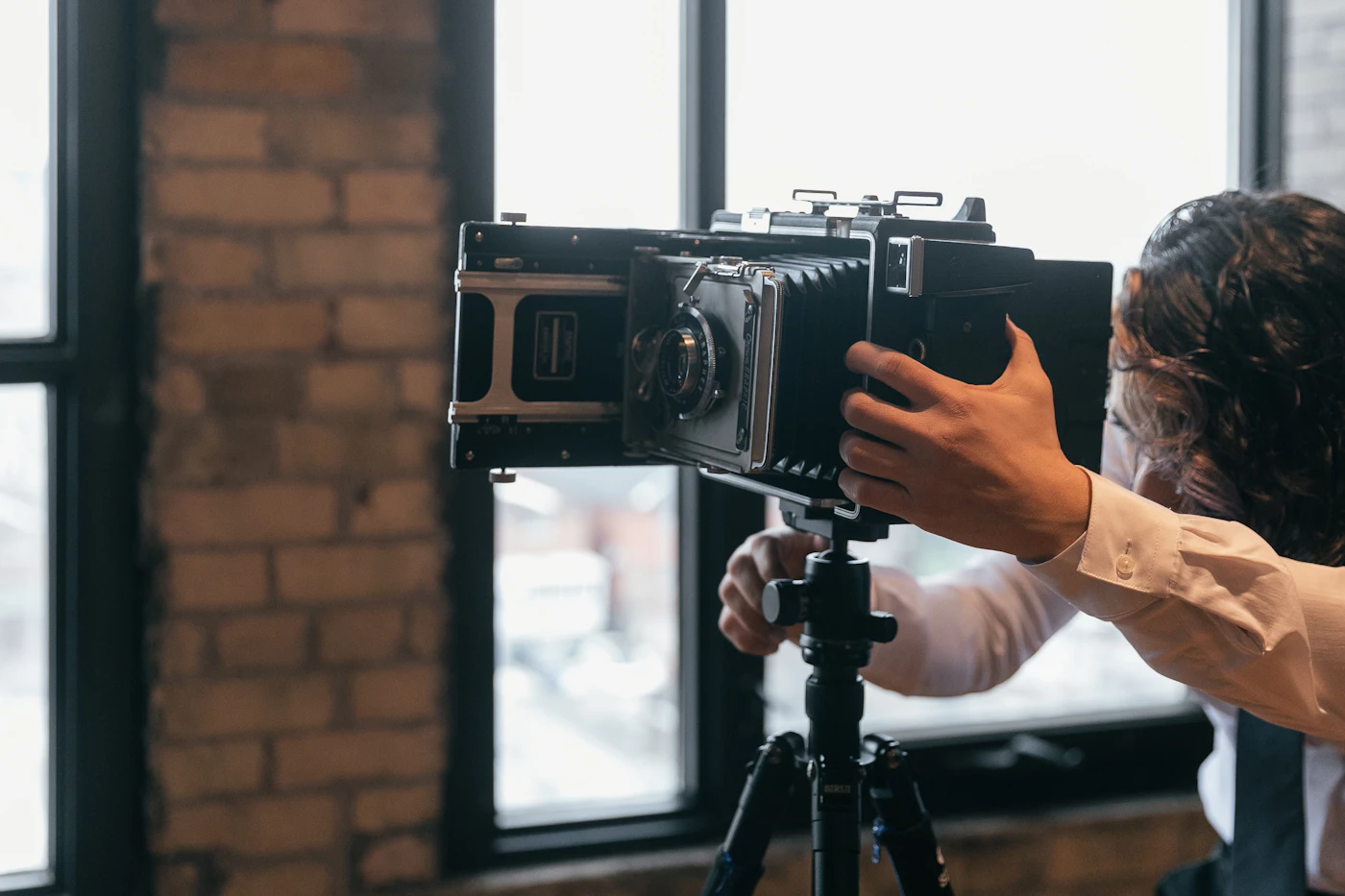 A person adjusting a large bellows camera on a tripod by a window