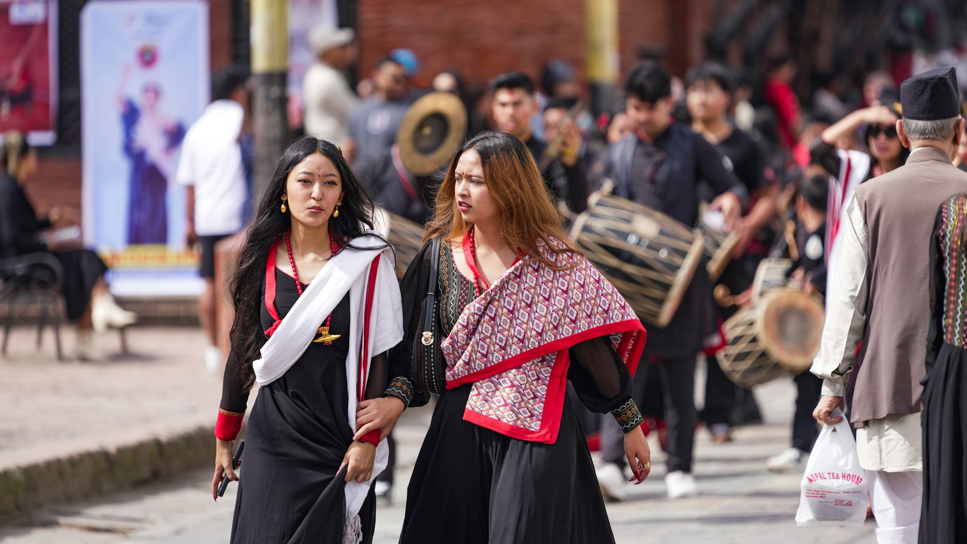 Two women in traditional attire walk in a procession.