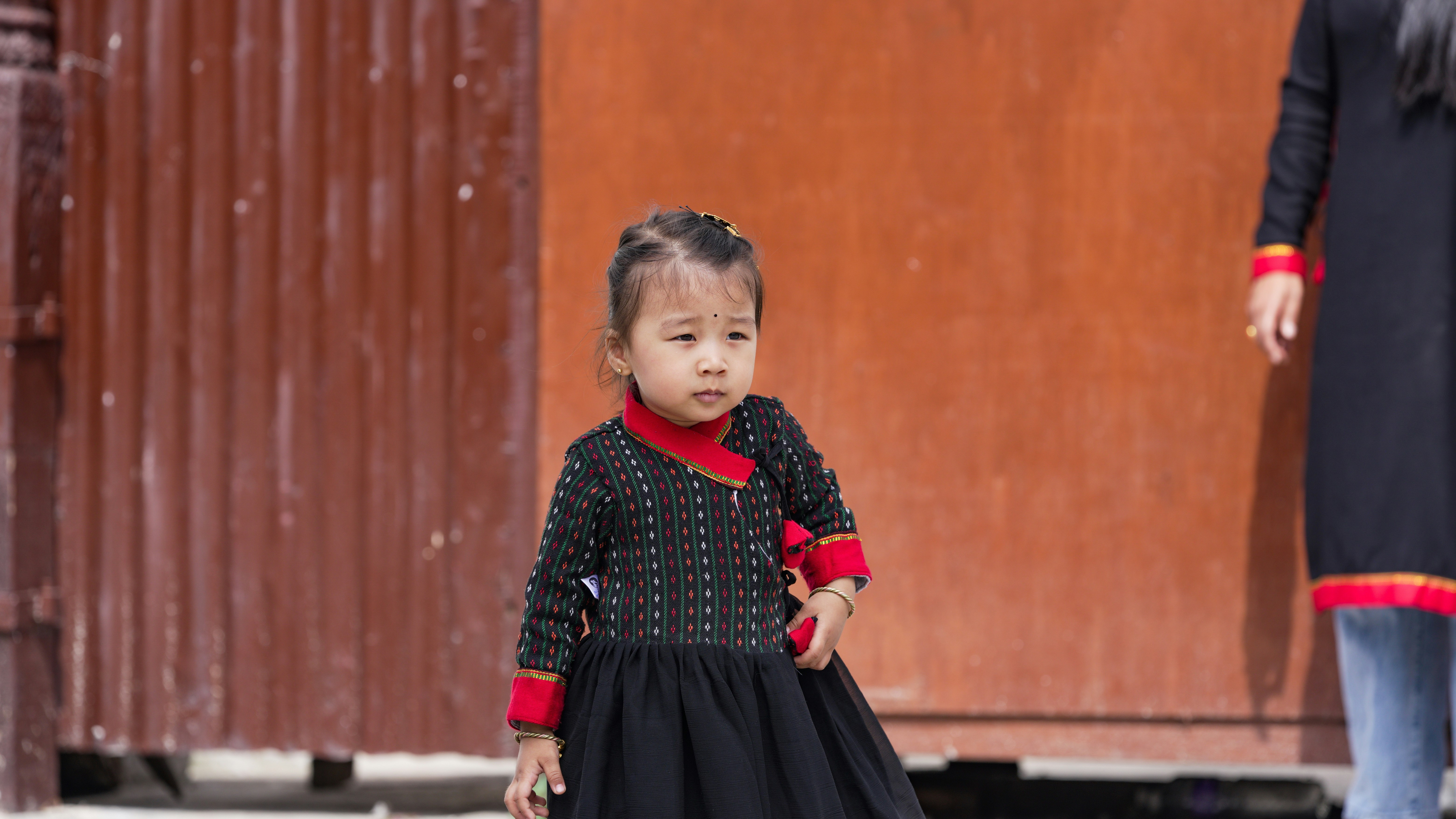 Young girl in traditional clothing stands near wall