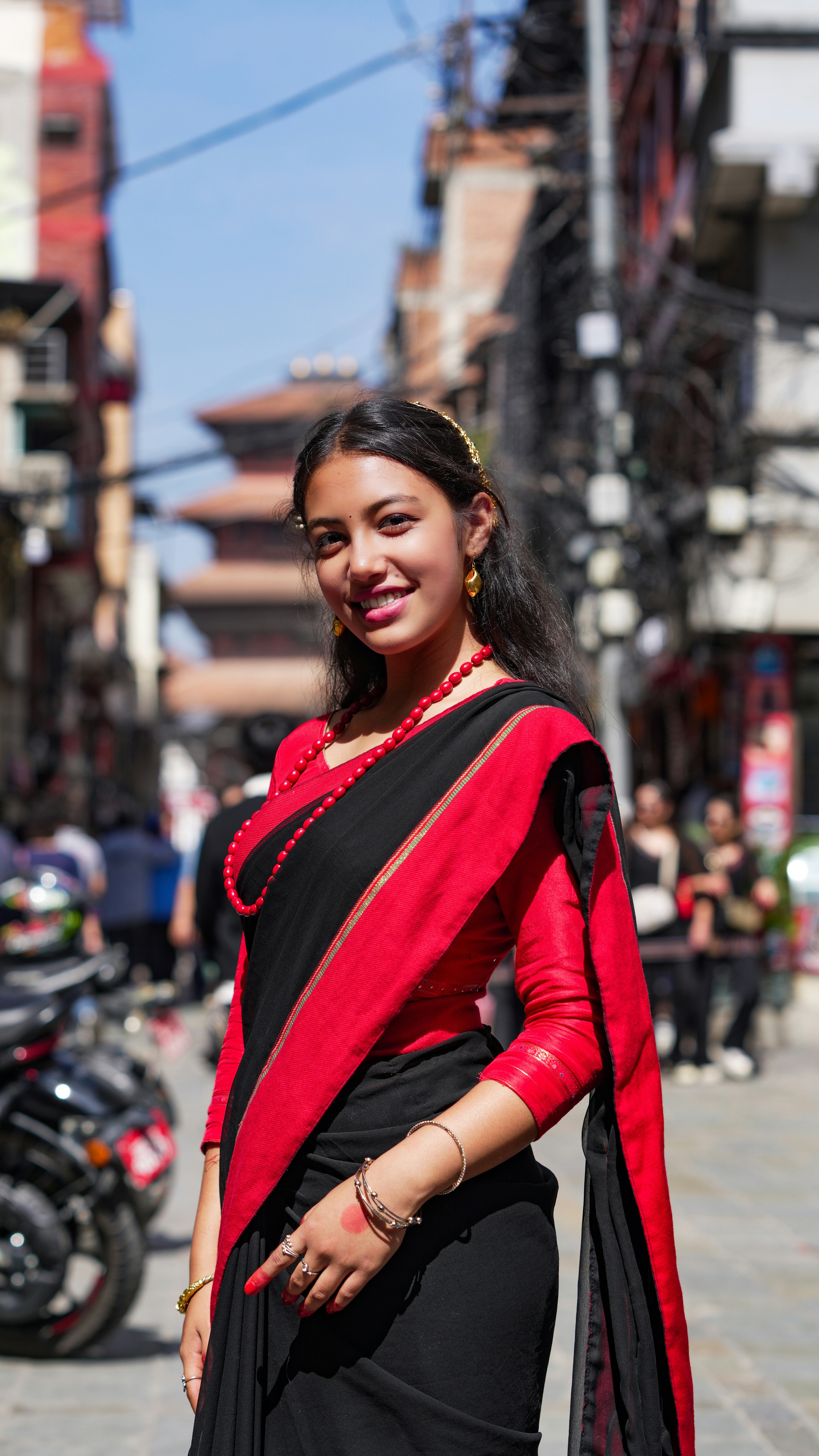 Young woman in traditional red and black sari smiles outdoors.