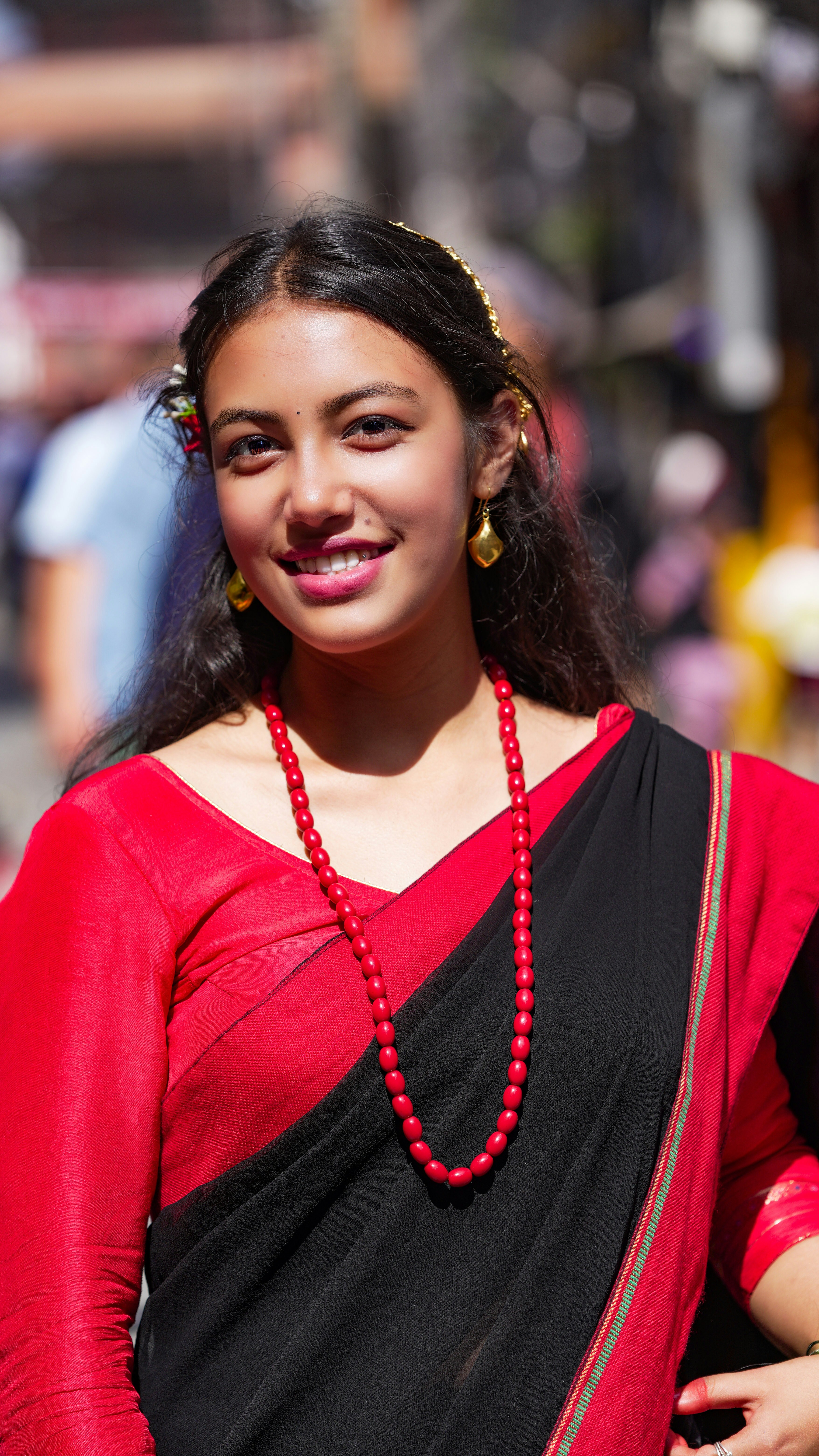 Young woman in traditional red and black sari smiling.