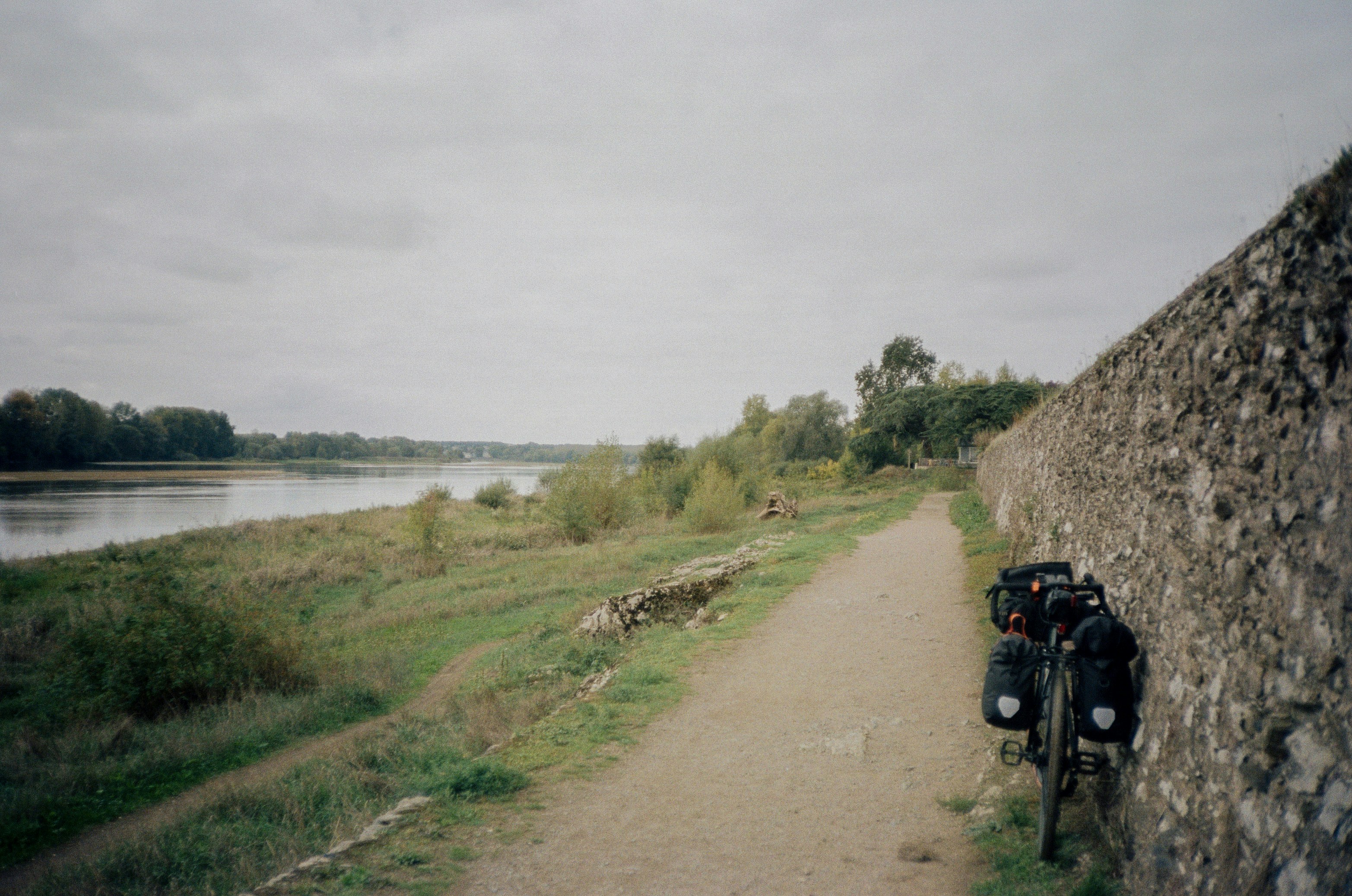Bicycle parked by stone wall next to river path