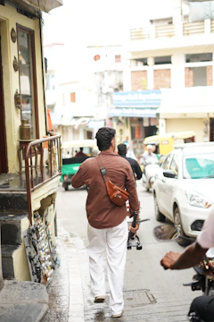 Man walking down a narrow street with vehicles.