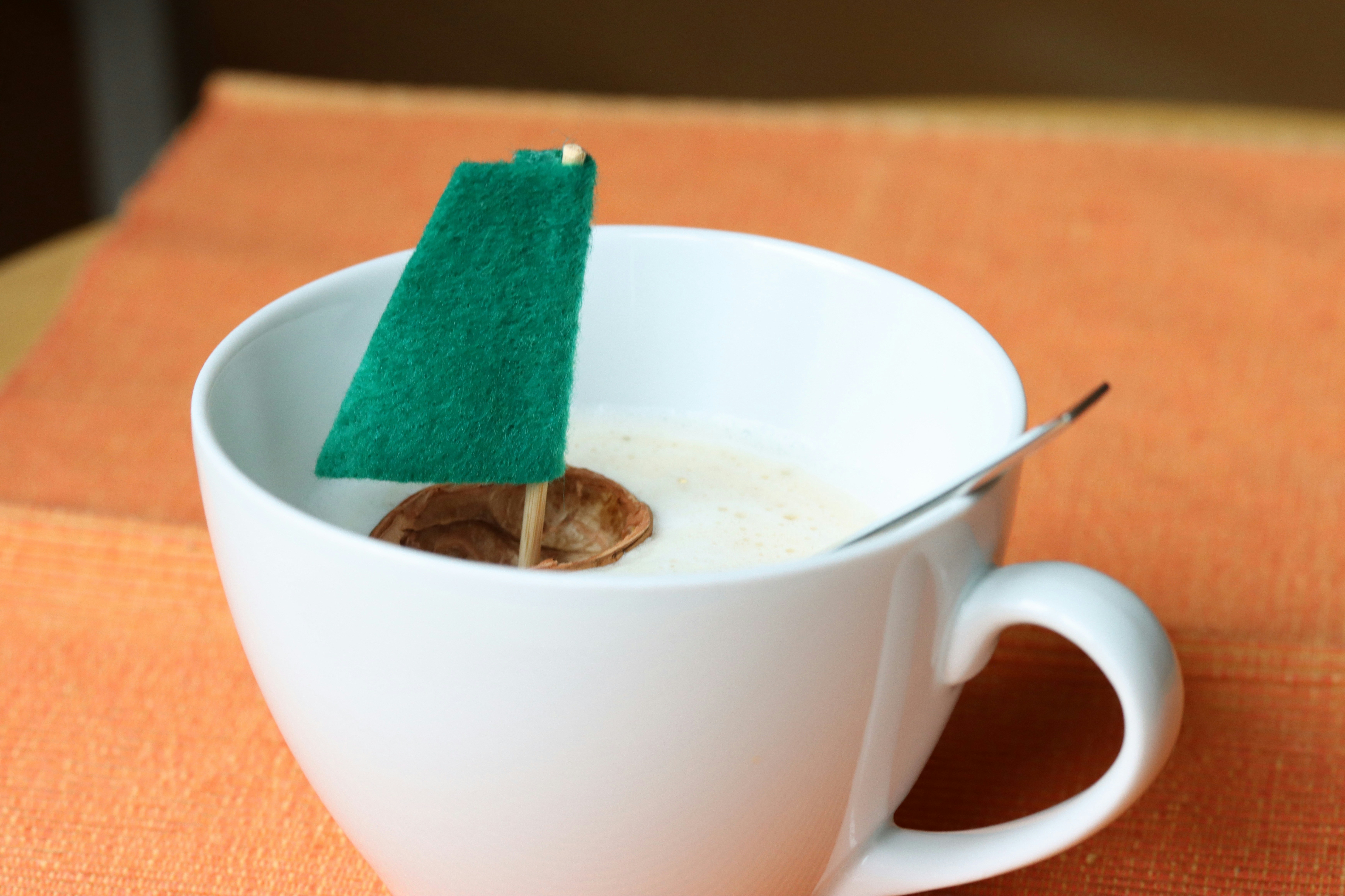 A tiny green sailboat in a white coffee cup.