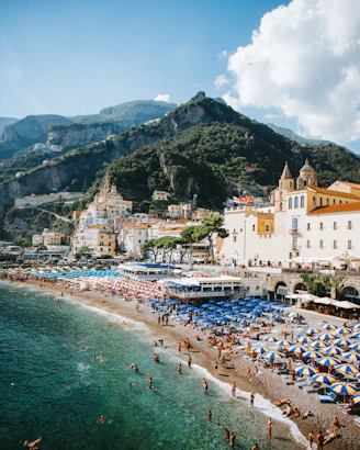 Crowded beach with umbrellas and buildings on a sunny day.